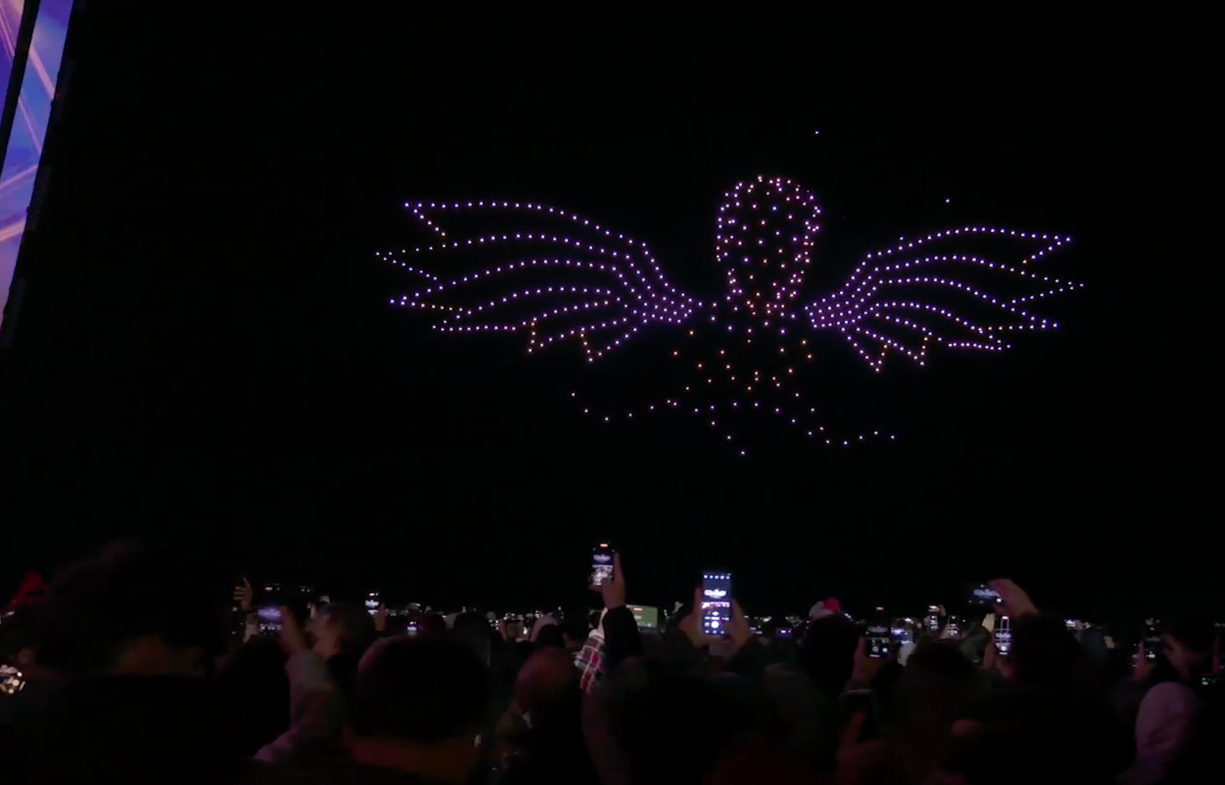 Un spectacle de lumière drones led  au dessus de la mer Méditérranée montrant un ange en LED drones violet sur un ciel noir  vu par un grand public de 230000 spectateurs au Portugal qui filme avec leurs téléphones.
