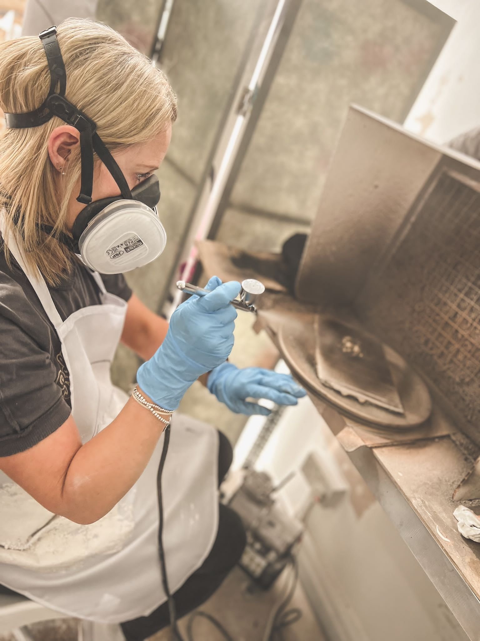 Person wearing a respirator, gloves, and apron using an airbrush tool
