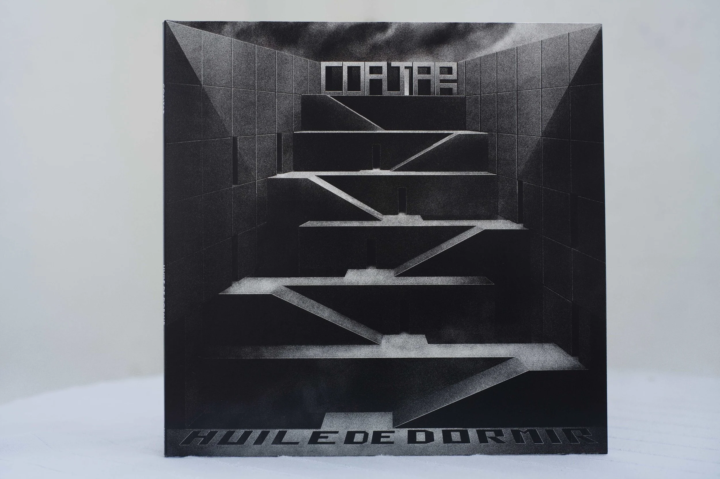 La face avant de l'album vinyle Huile de Dormir du groupe Coaltar, c'est un dessin en noir et blanc représentant une structure brutaliste avec des rampes montant du premier plan au troisieme plan, le nom du groupe et de l'album apparaissent 