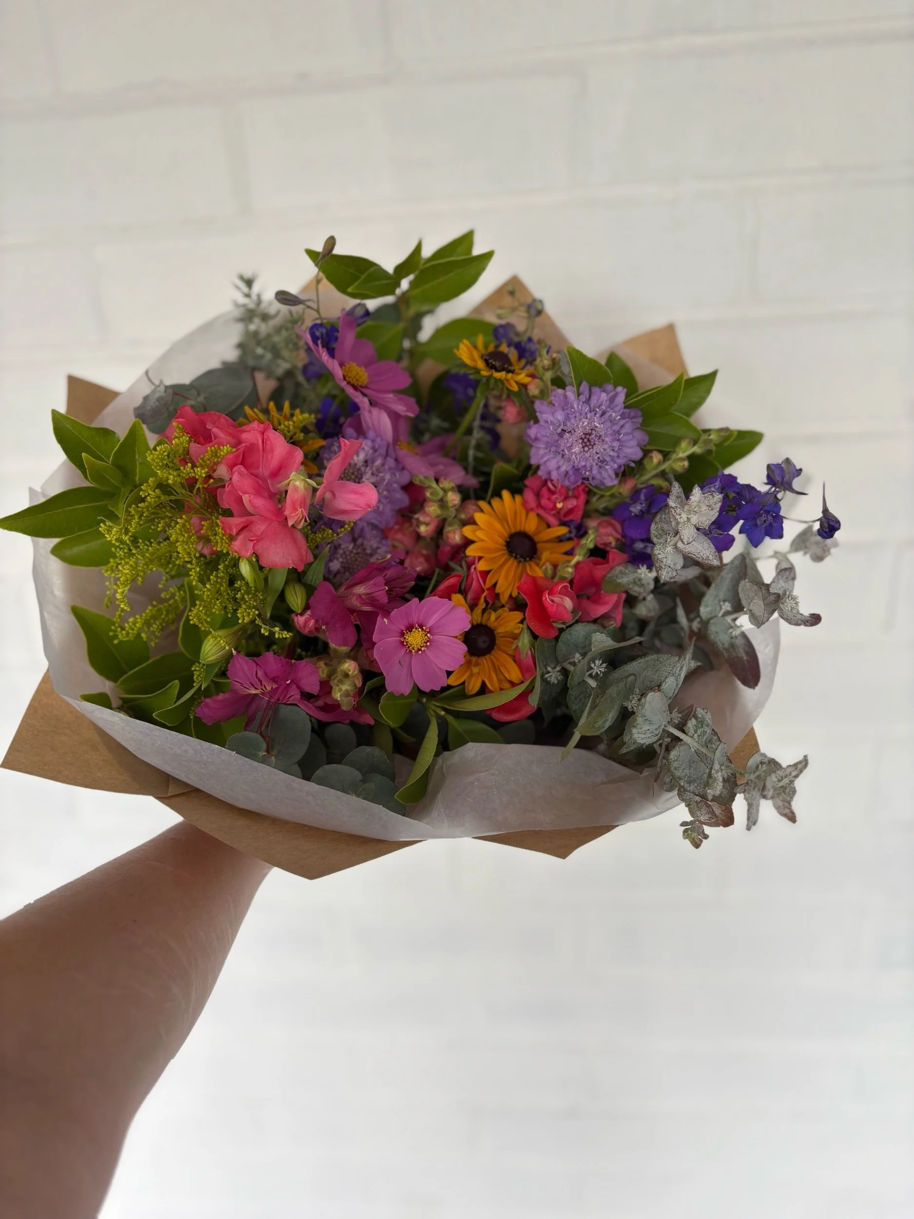 A cottage garden style posy bouquet of mixed seasonal flowers in bright tones.