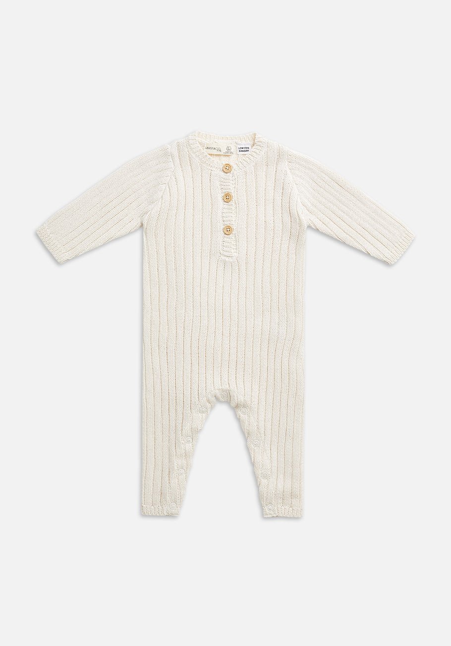 Cream-colored knitted baby romper with long sleeves, ribbed texture, and four buttons down the front