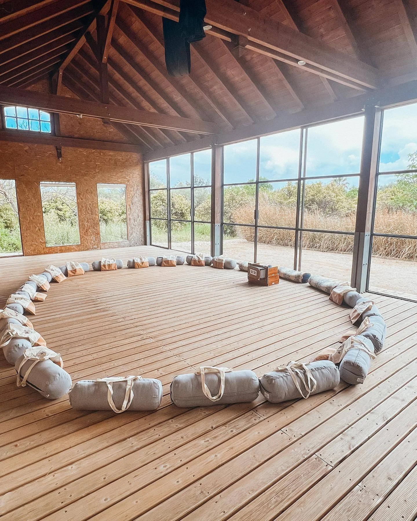 Inside a wooden structure with large glass windows, arranged in a circle on a wooden floor, are sky lanterns or paper lanterns, with some equipment and boxes nearby.