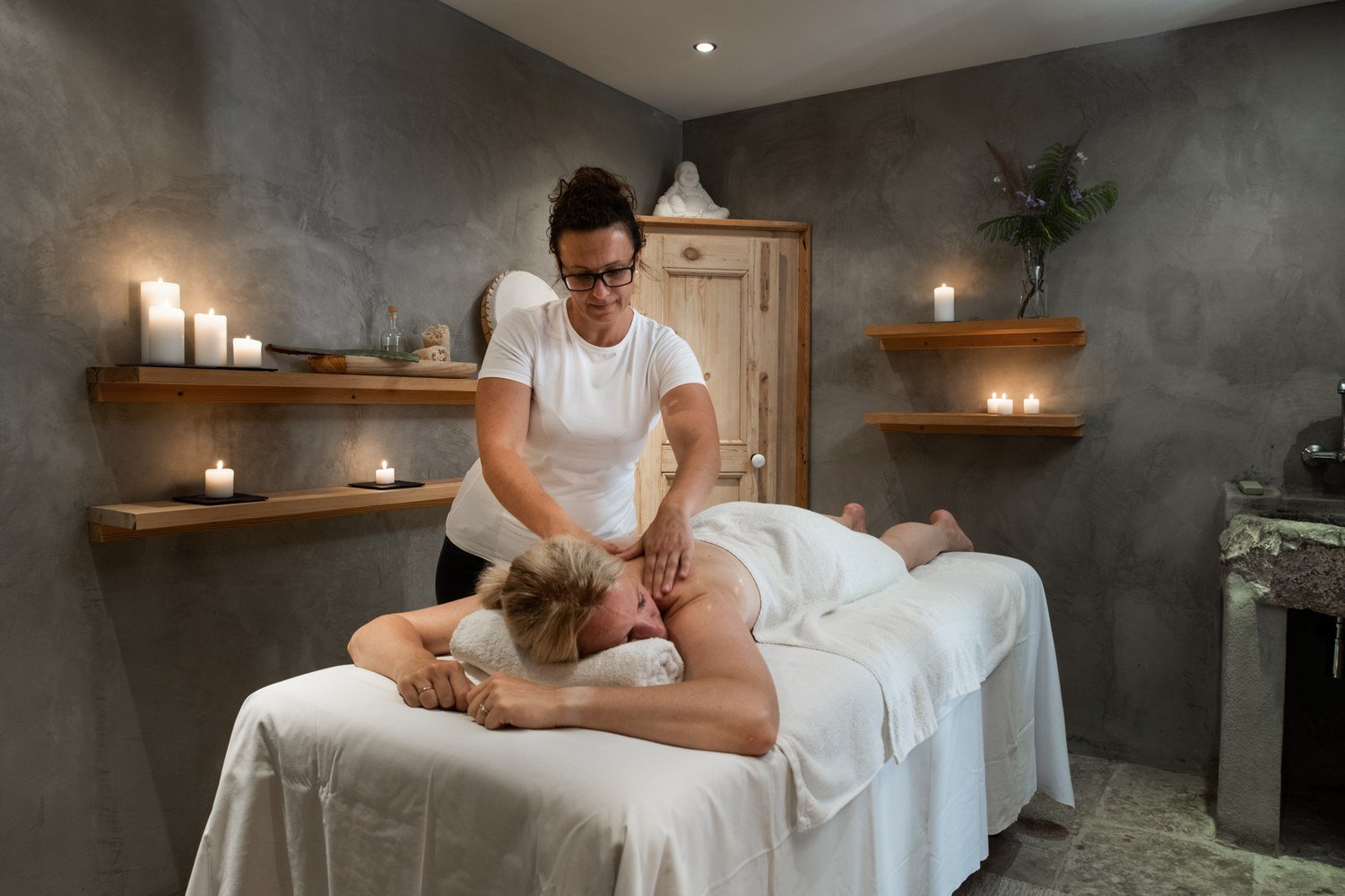 A woman receives a massage in a dimly lit room decorated with candles and plants.