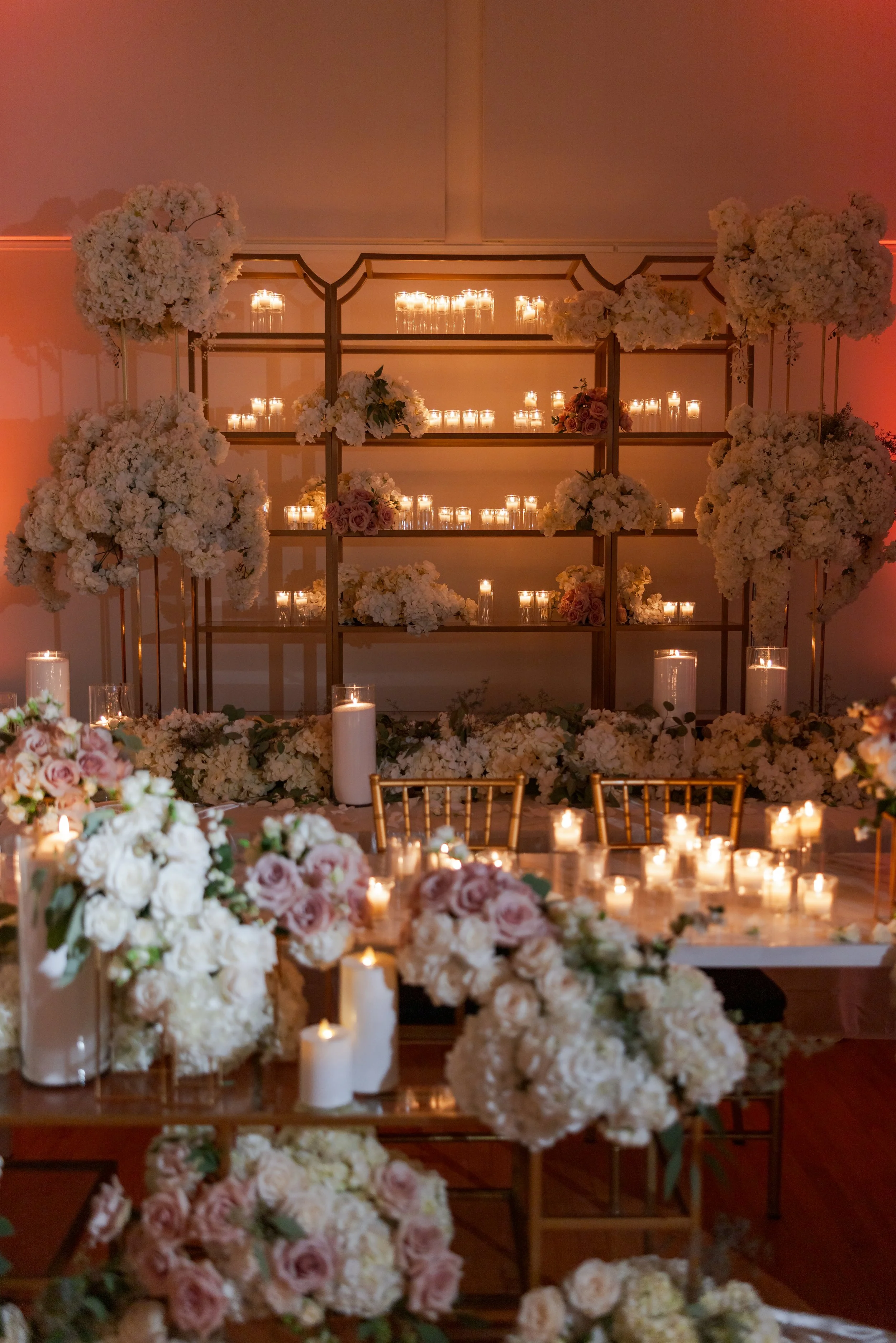 Elegant event decorated with cream and blush flower arrangements, candlelit lanterns, and a wooden backdrop for a wedding or celebration.