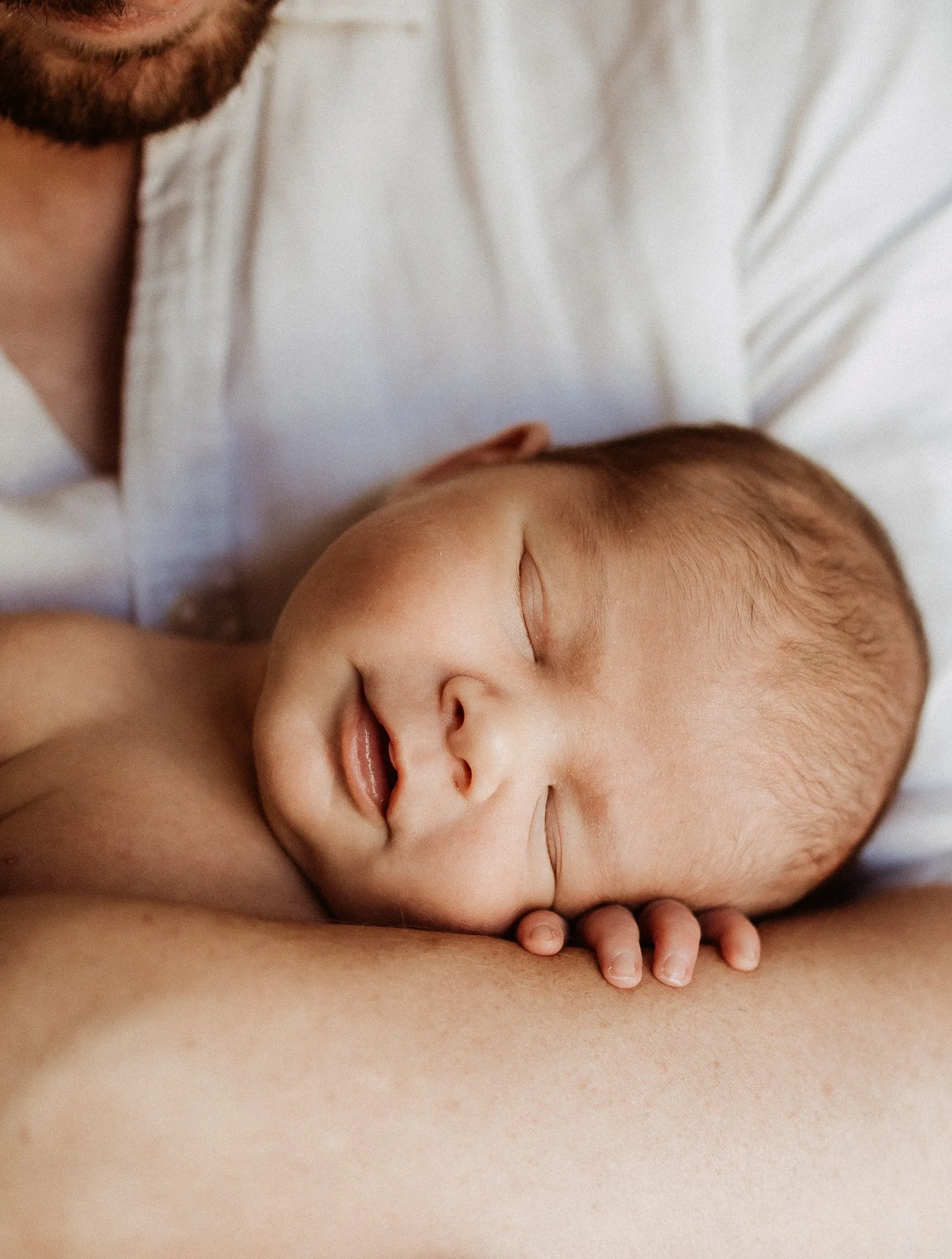 Close-up of a sleeping baby resting peacefully on someone's chest, with the person's hand gently supporting the baby's head.