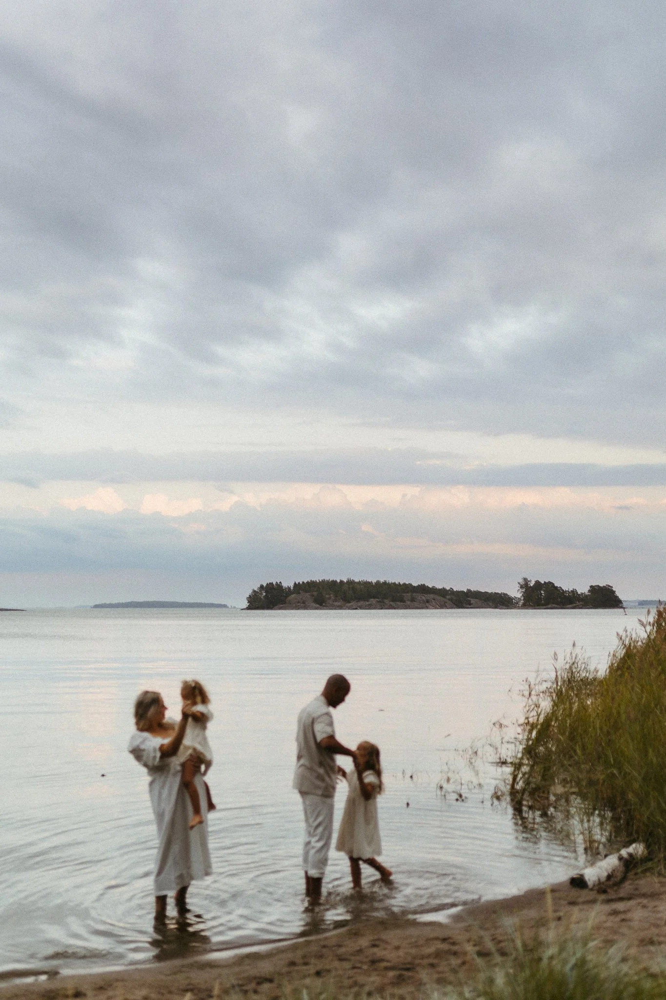 Family of four enjoying time by a lake with an island in the background, under a cloudy sky.