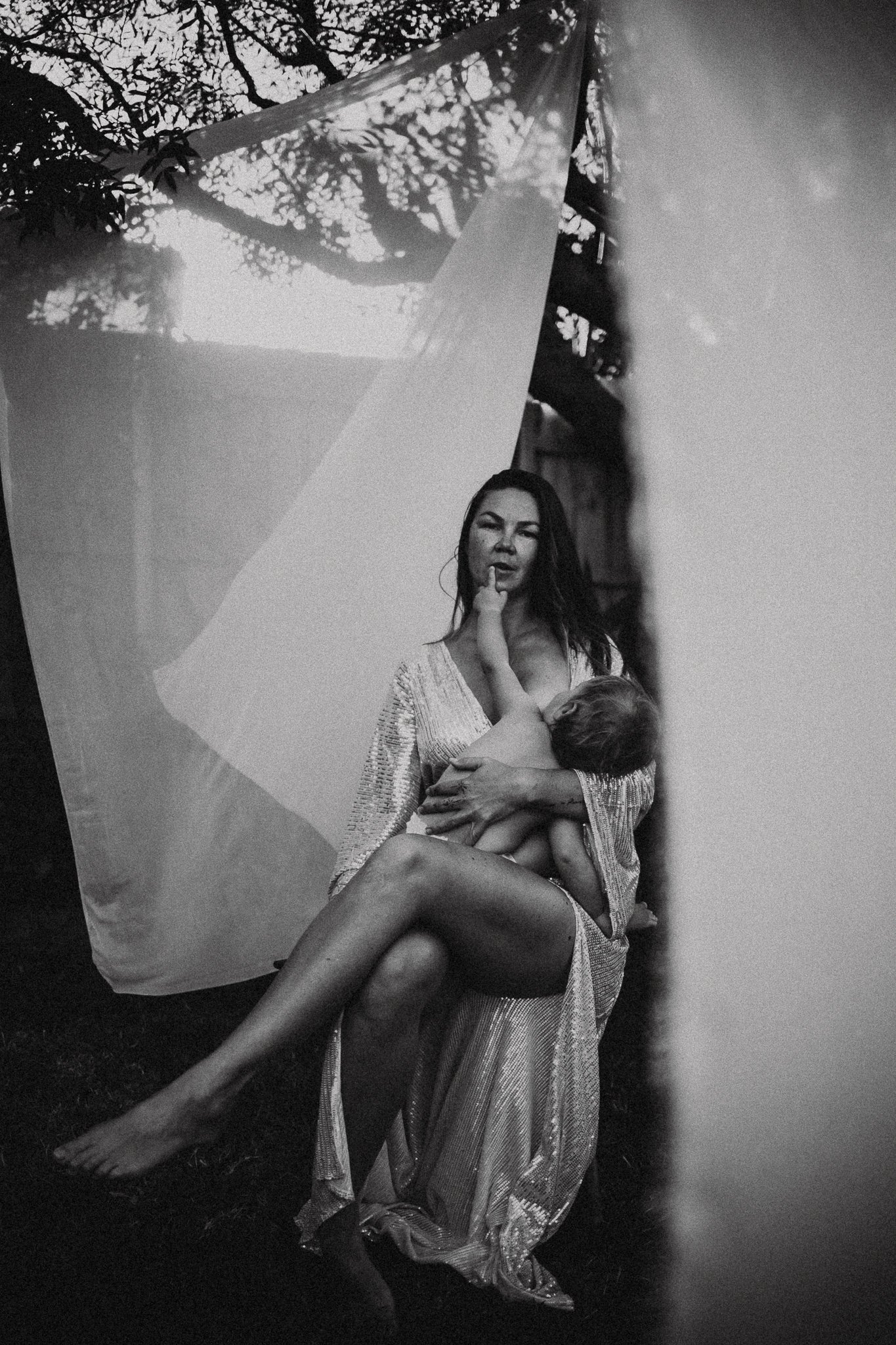 A woman holding a child, with the woman making a finger gesture to her lips, seen through a semi-transparent curtain."}