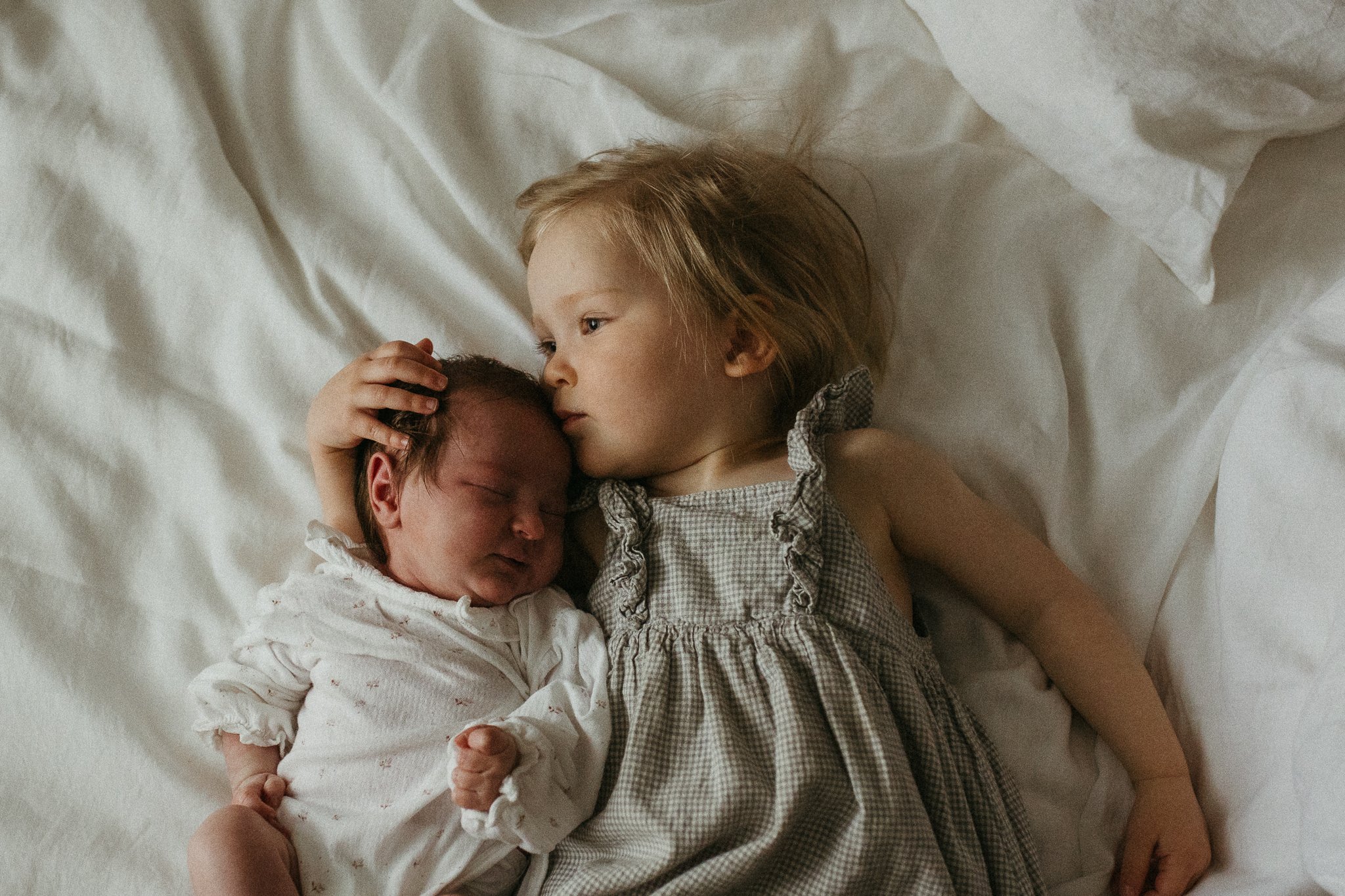 A young girl holding a newborn baby on a bed with white sheets.