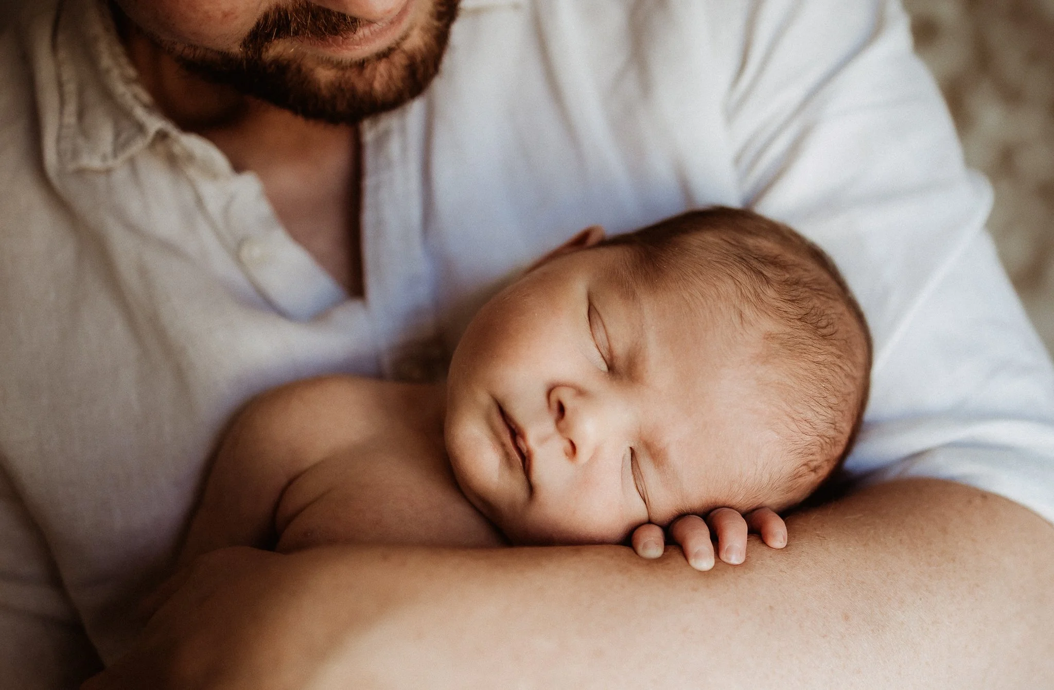 A close-up of a man lying down with a baby, both asleep, with the man holding the baby gently.
