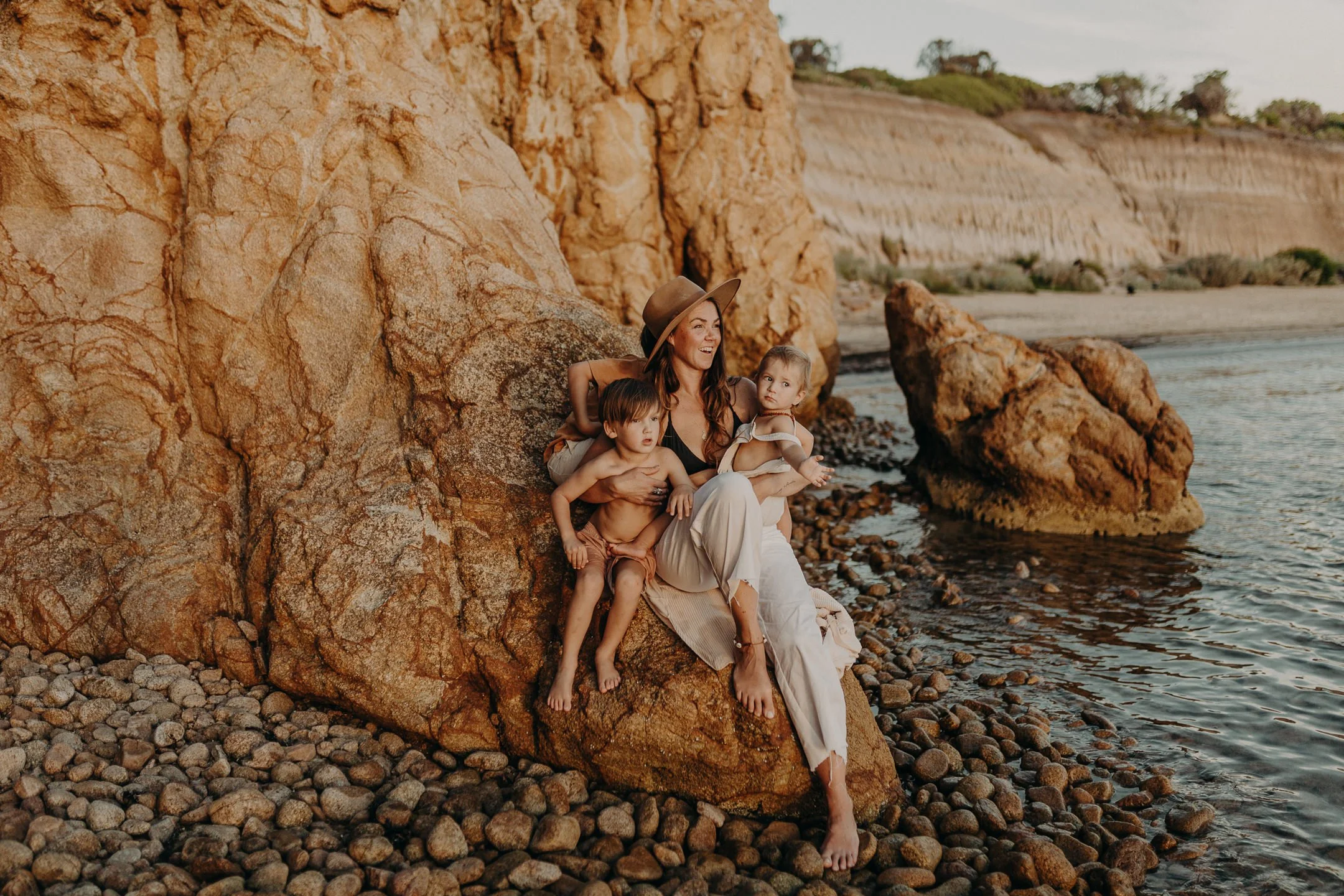 Woman and two children sitting on rocky beach beside cliffs