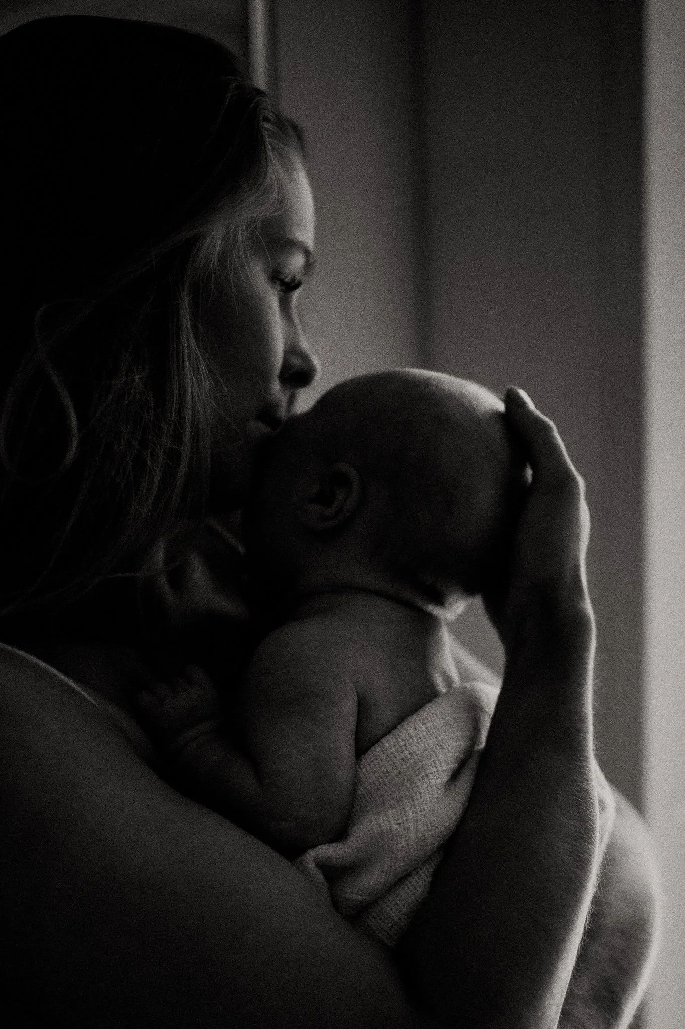 A woman with long hair holding a bald baby close to her face in black and white.