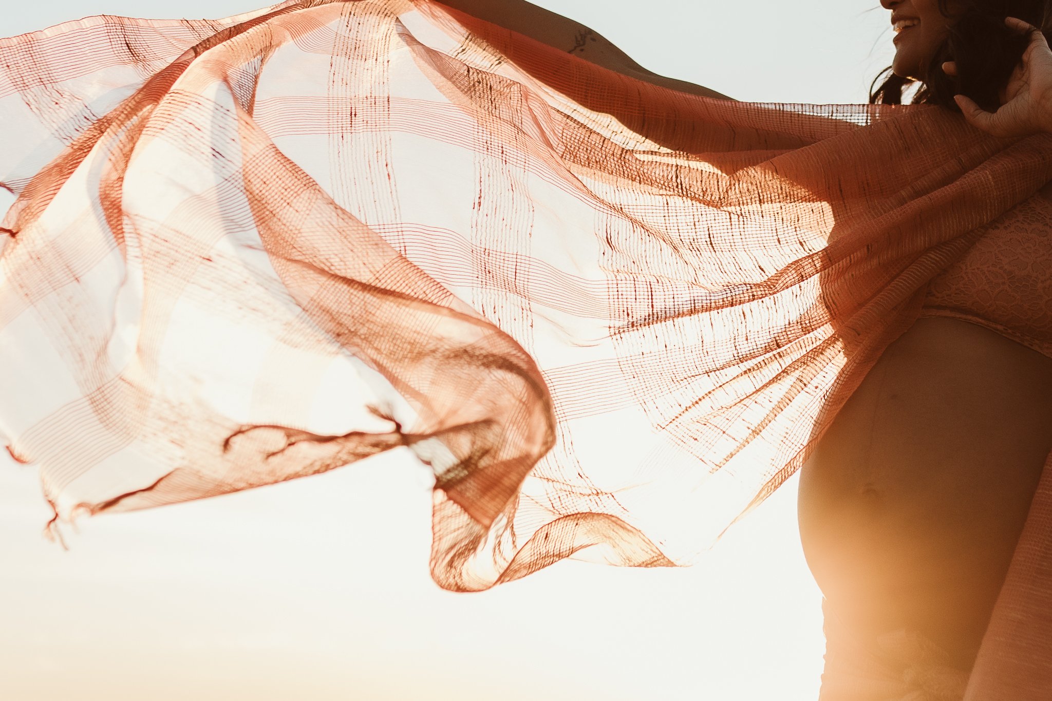 A woman holding a flowing, sheer orange fabric against a bright sky