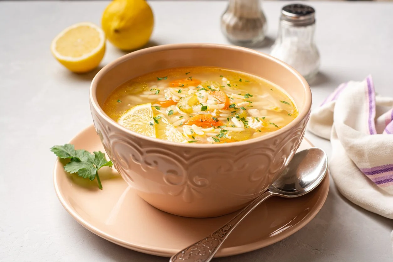 a hearty and zesty lemon chicken soup in a ceramic bowl with lemons in the backdrop with salt & pepper shakers