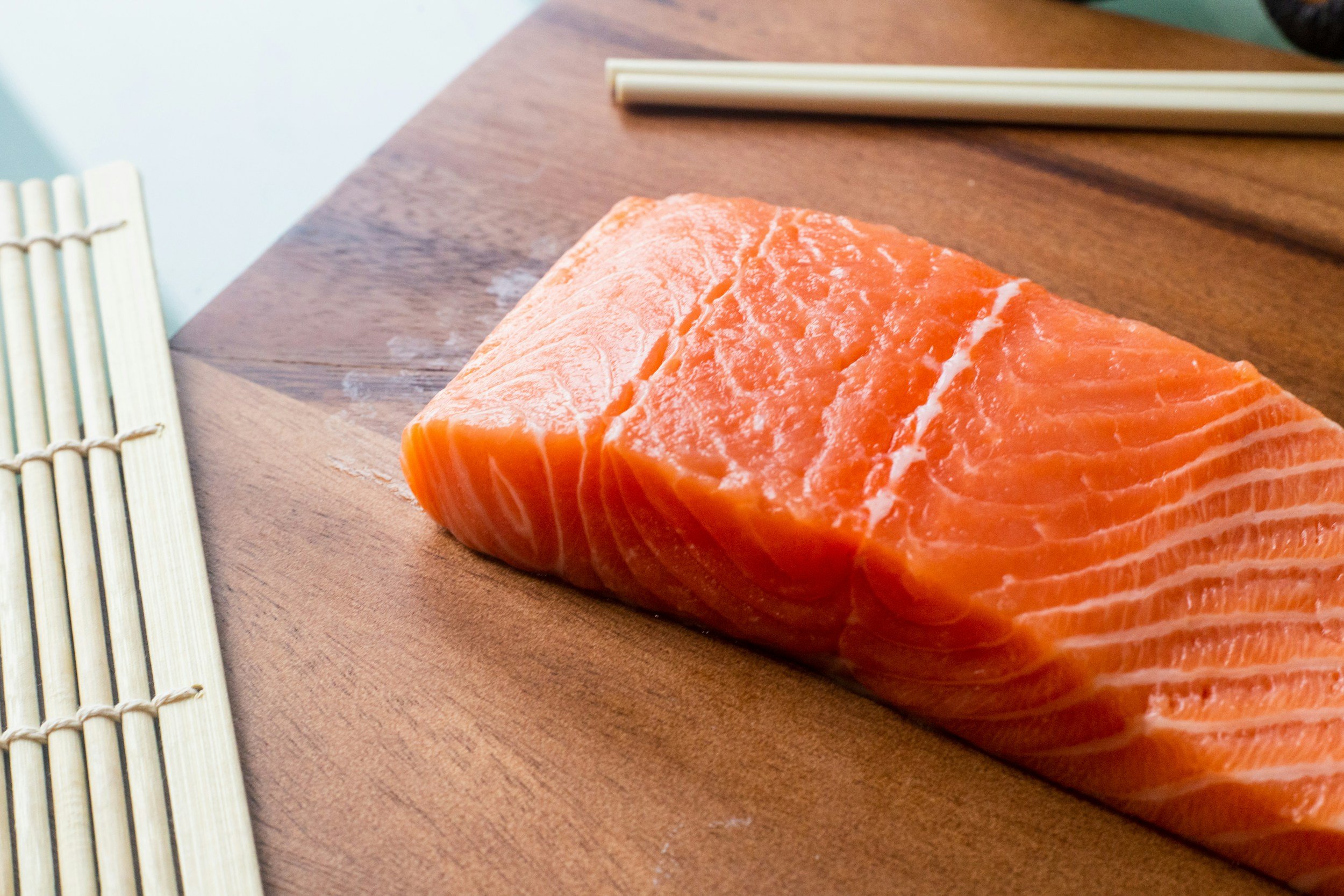 piece of salmon on a wooden cutting board with chopsticks
