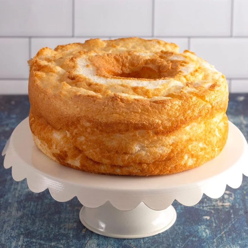 Angel food cake on a white cake stand with a blue background.