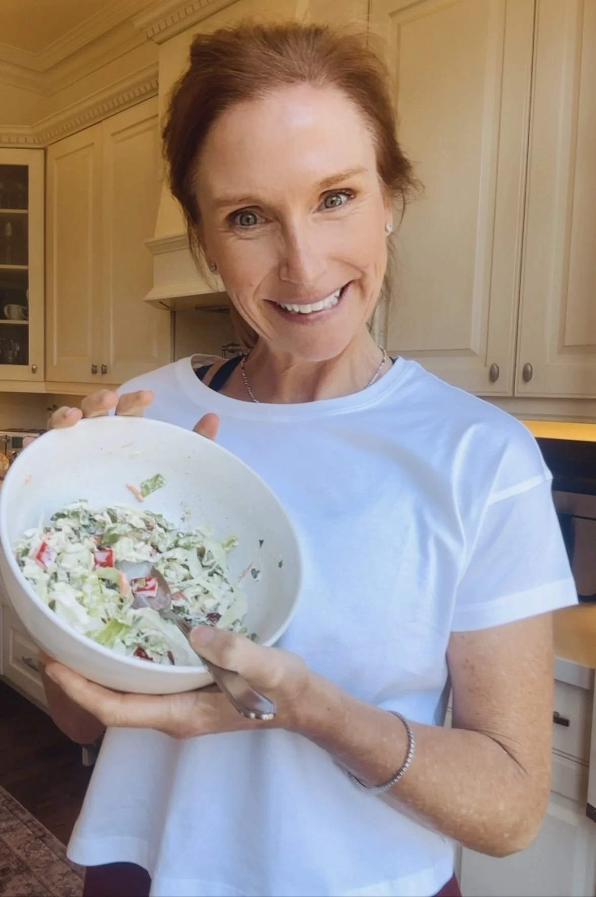 woman in white kitchen holding a bowl with salad