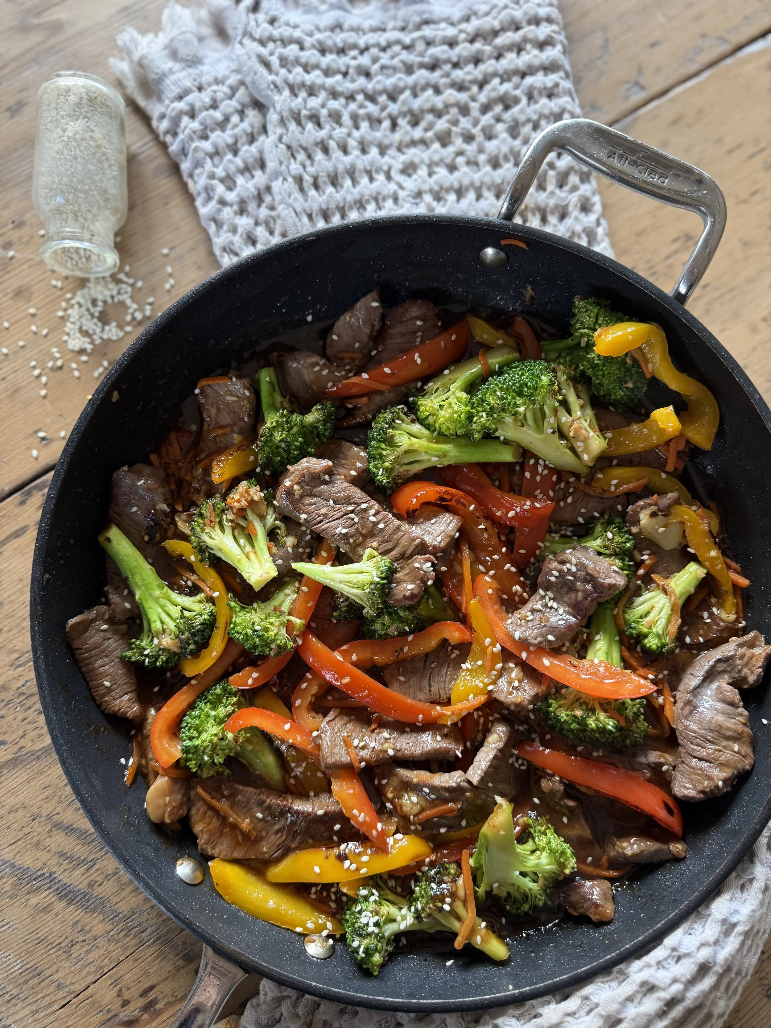 a skillet on a wooden table with bright veggies and juicy beef strips