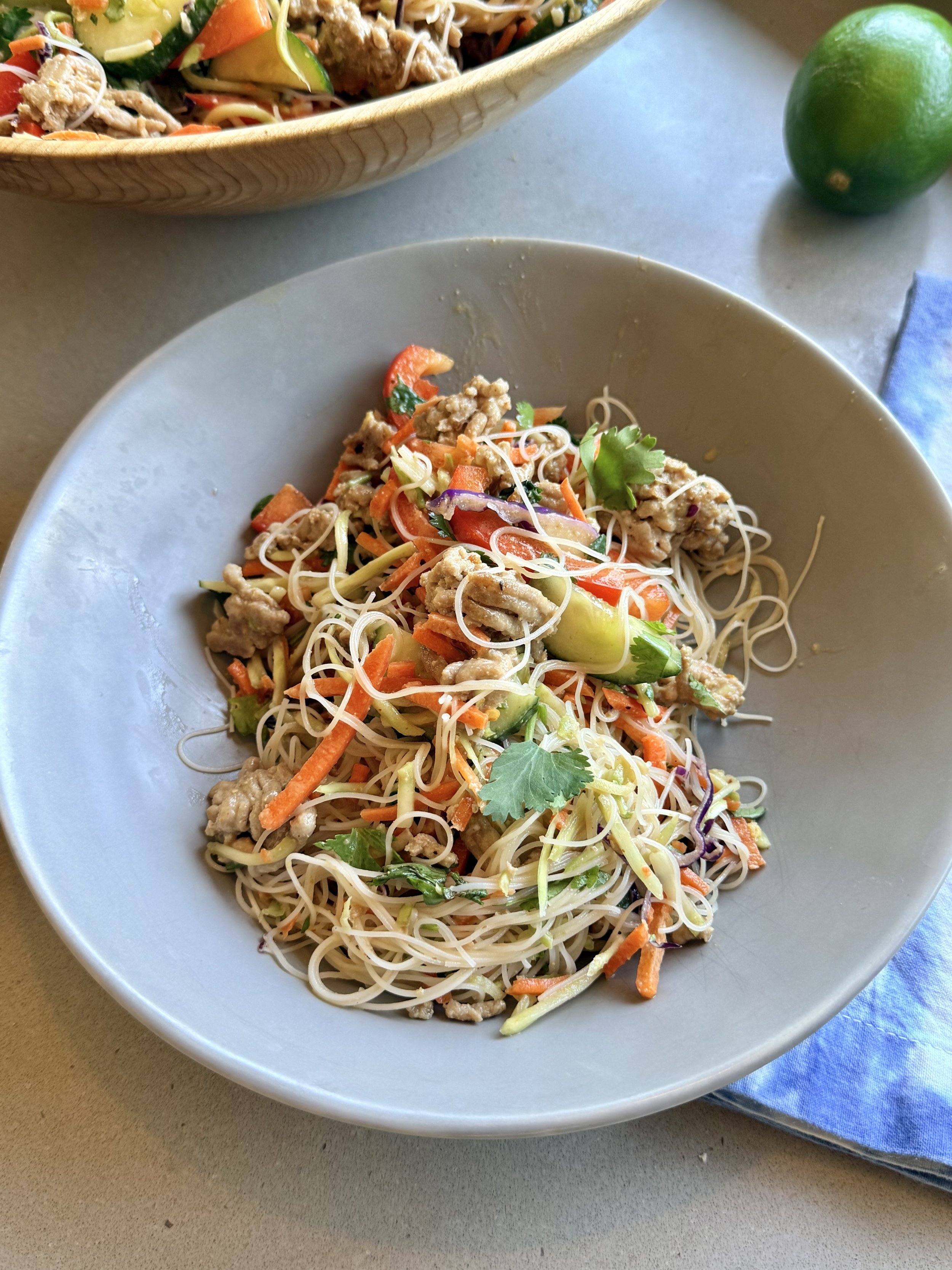 rice noodles, ground chicken, vegetables in a grey bowl with a lime in the background