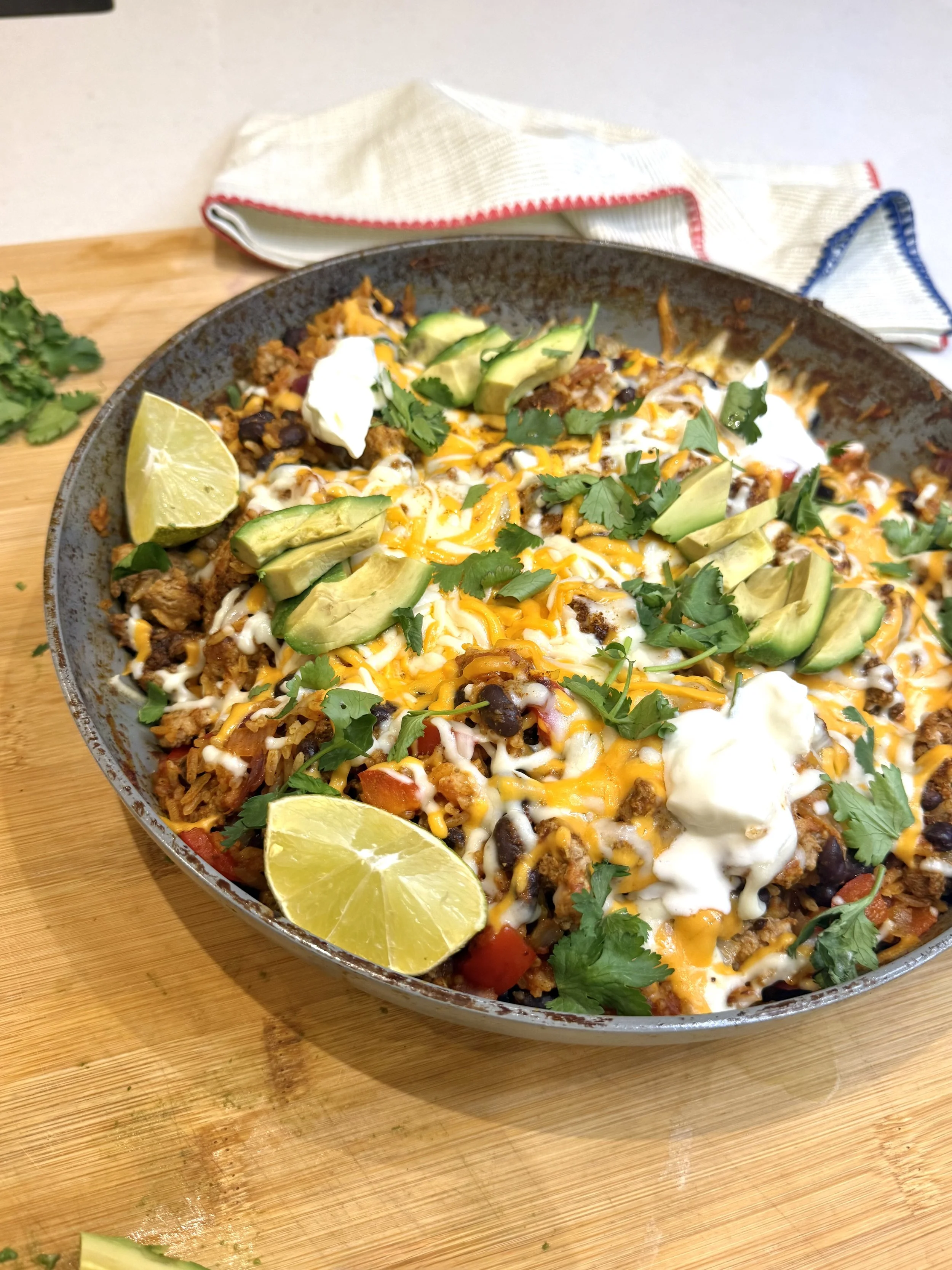 large skillet filled with turkey taco skillet, melted cheese, topped with avocado and cilantro