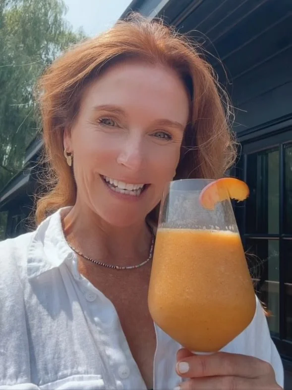 A delicious peach mocktail (or cocktail!) using frozen peaches and non-alcoholic wine in a wine glass, garnished with fresh peach