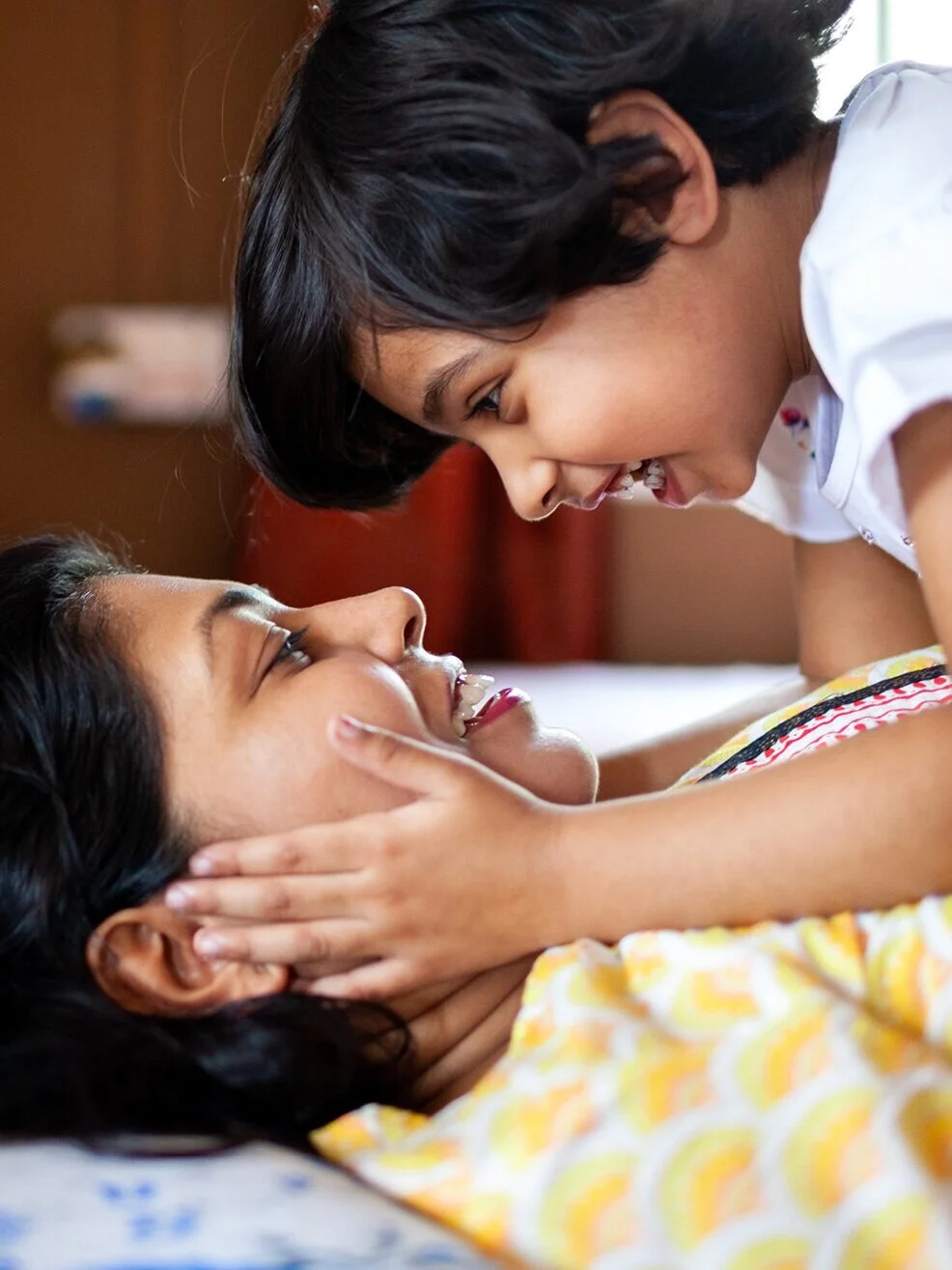 A joyful young girl and woman share a close, playful moment together indoors.