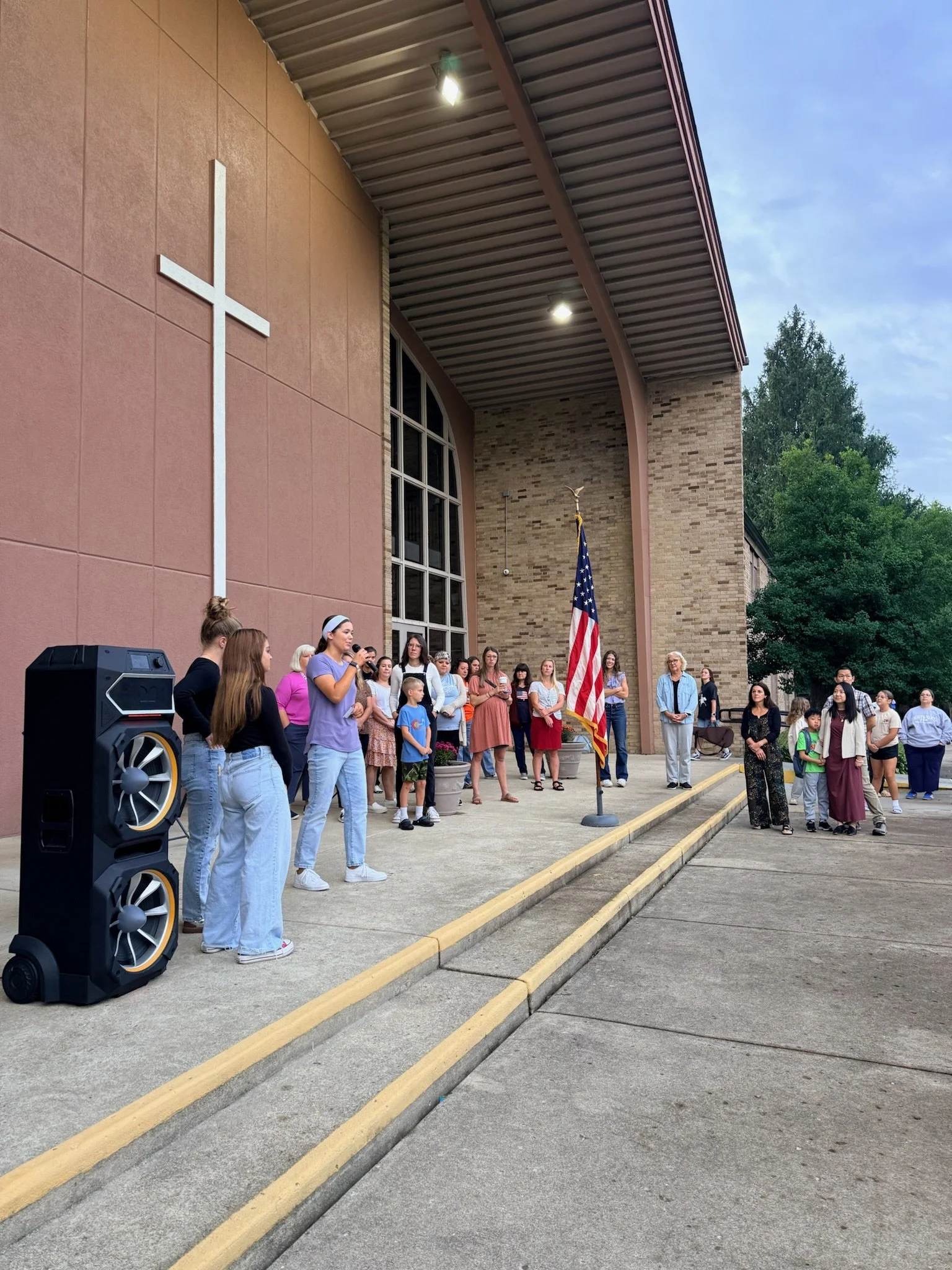 A group of young children sitting and kneeling on a rug in a classroom, looking at pink folders.