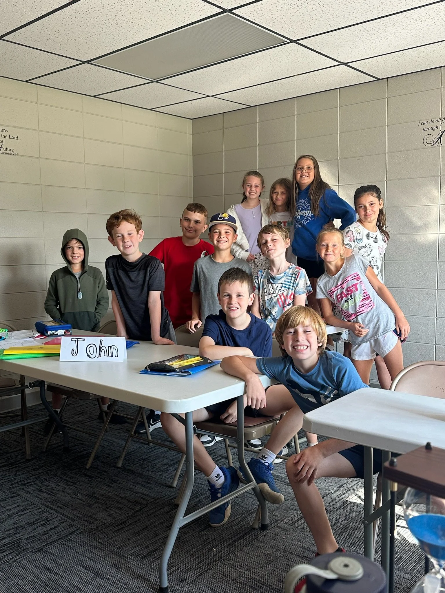 Three girls with light skin posing together in front of a wooden backdrop, celebrating fall, with pumpkins, sunflowers, and autumn decor around them.