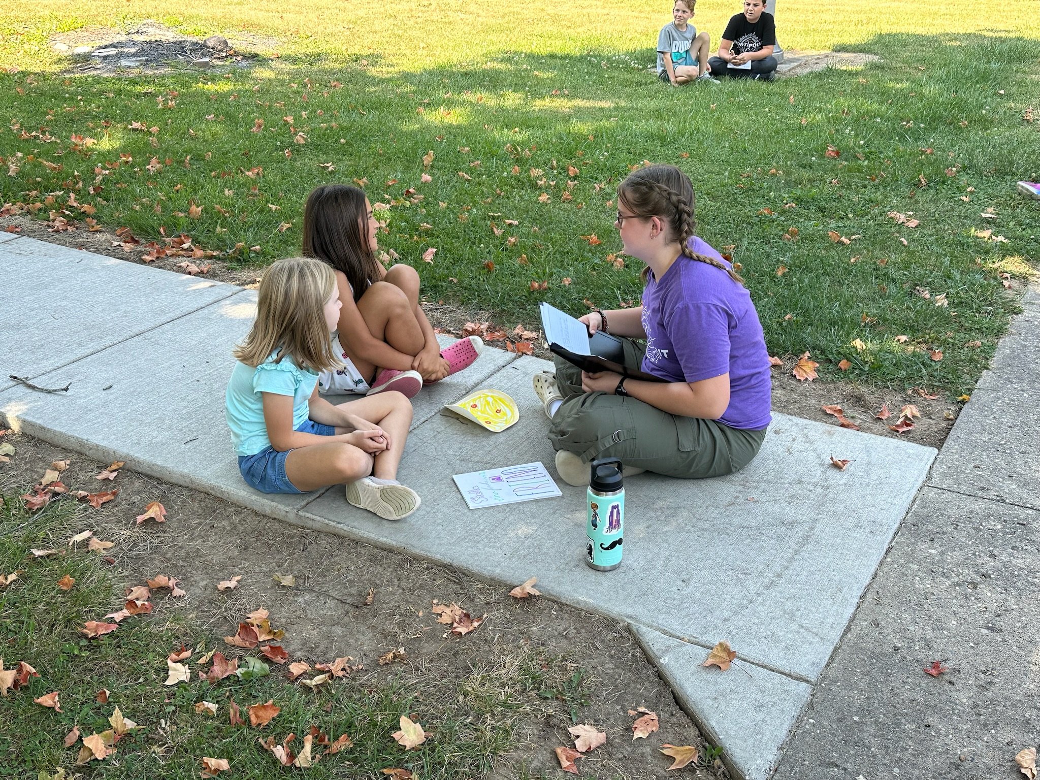 A large group of students seated in an auditorium, many raising their hands, during a school assembly or presentation.
