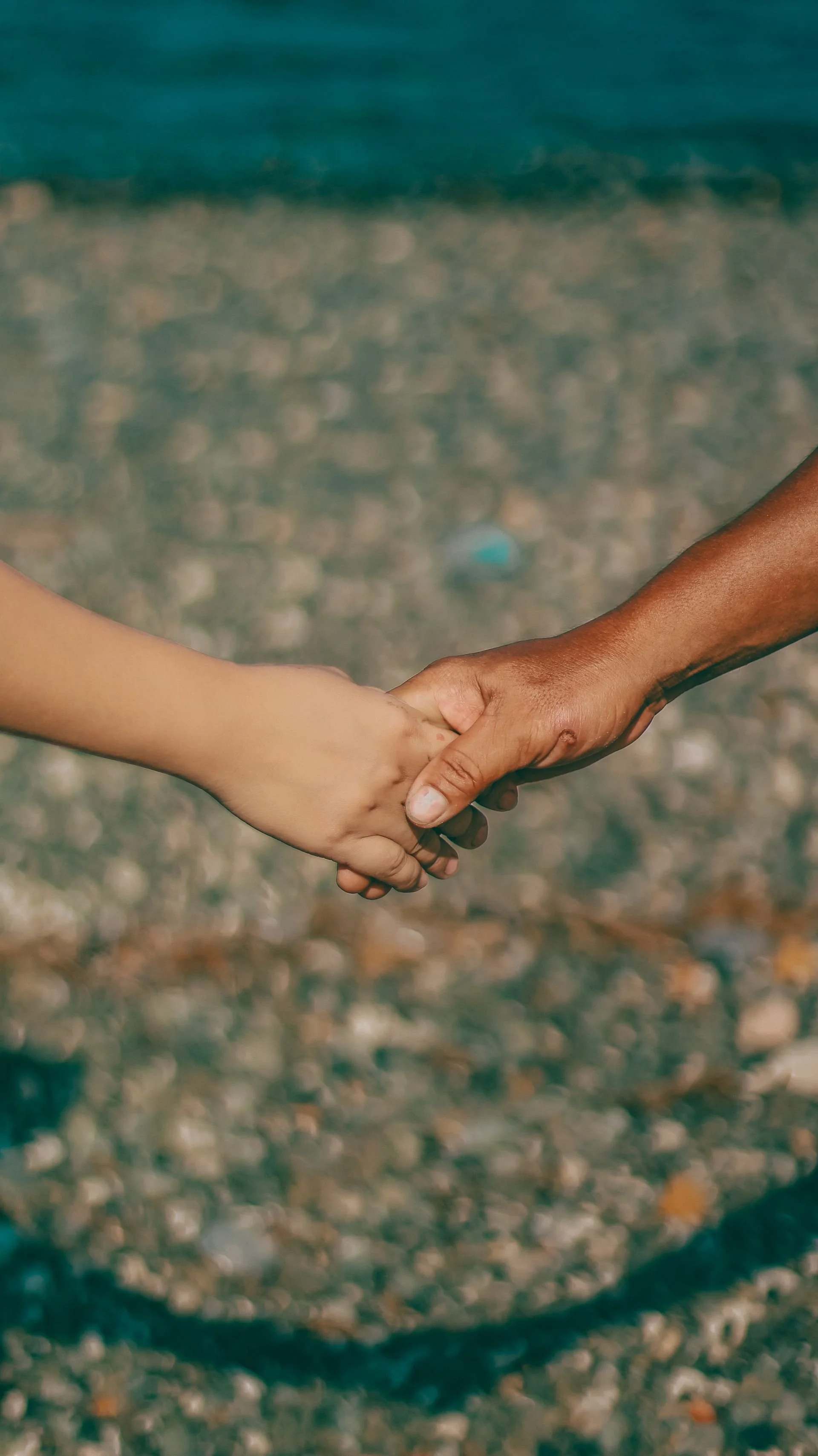 Two people holding hands, one with light skin and the other with dark skin, on a sandy beach.