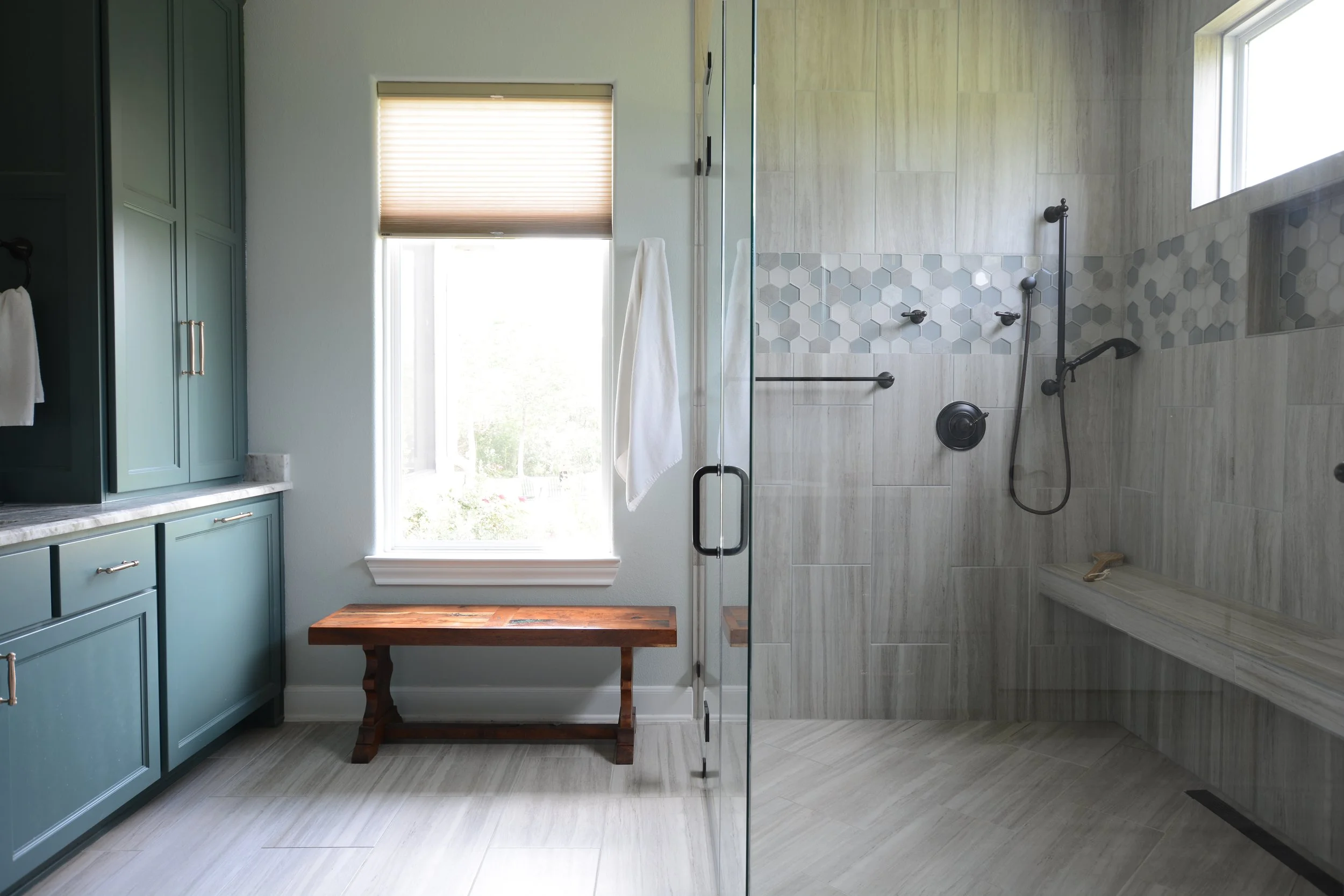 Modern bathroom with teal cabinetry, a large window, and a walk-in shower with neutral tiles and a bench.