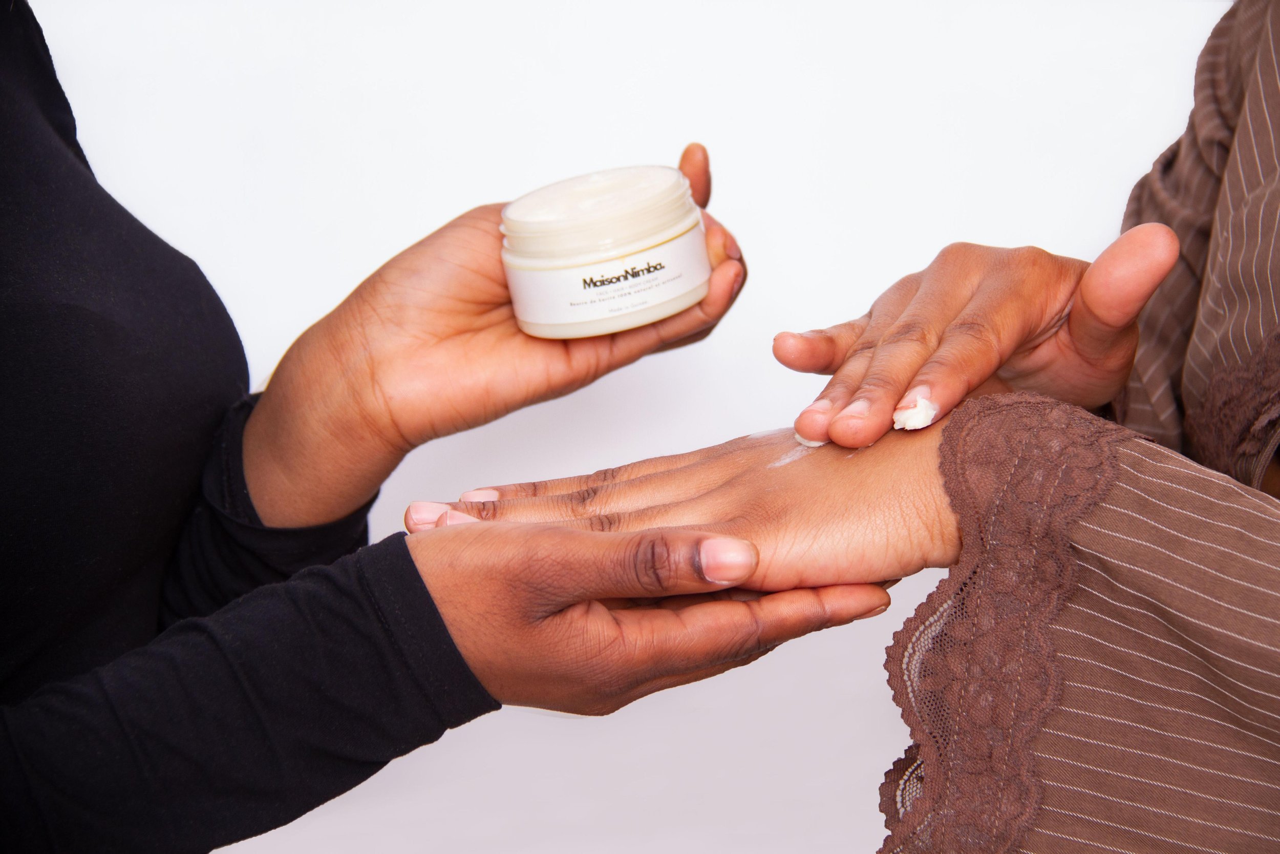 Une personne applique une crème sur la main d'une autre personne dans un contexte de soin ou de beauté.