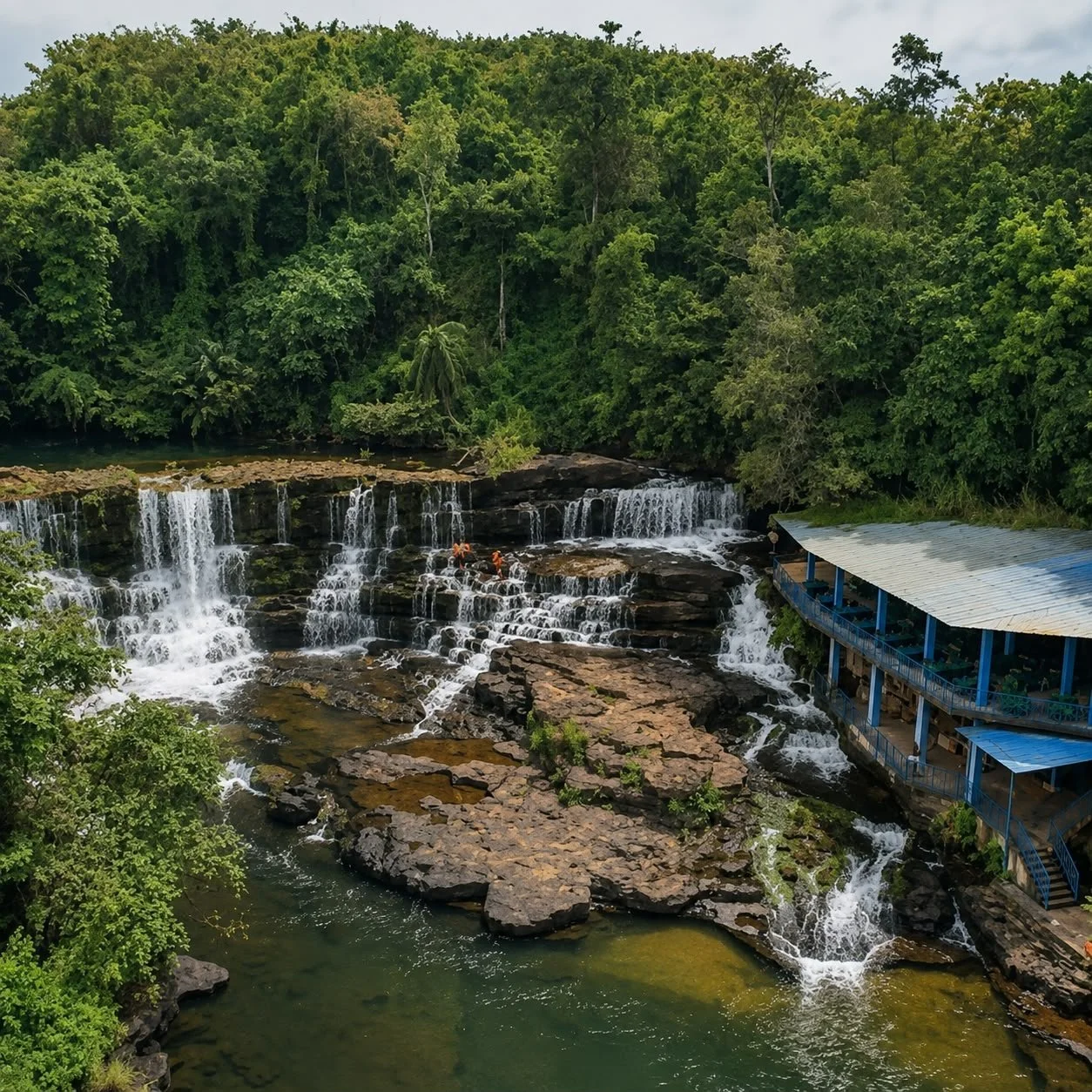 Cascade d'eau dans une forêt dense avec un bâtiment en bois bleu sur le côté droit.