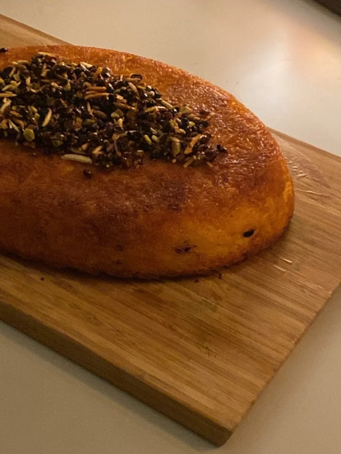 A baked loaf of bread topped with chopped herbs and seeds, resting on a wooden cutting board.