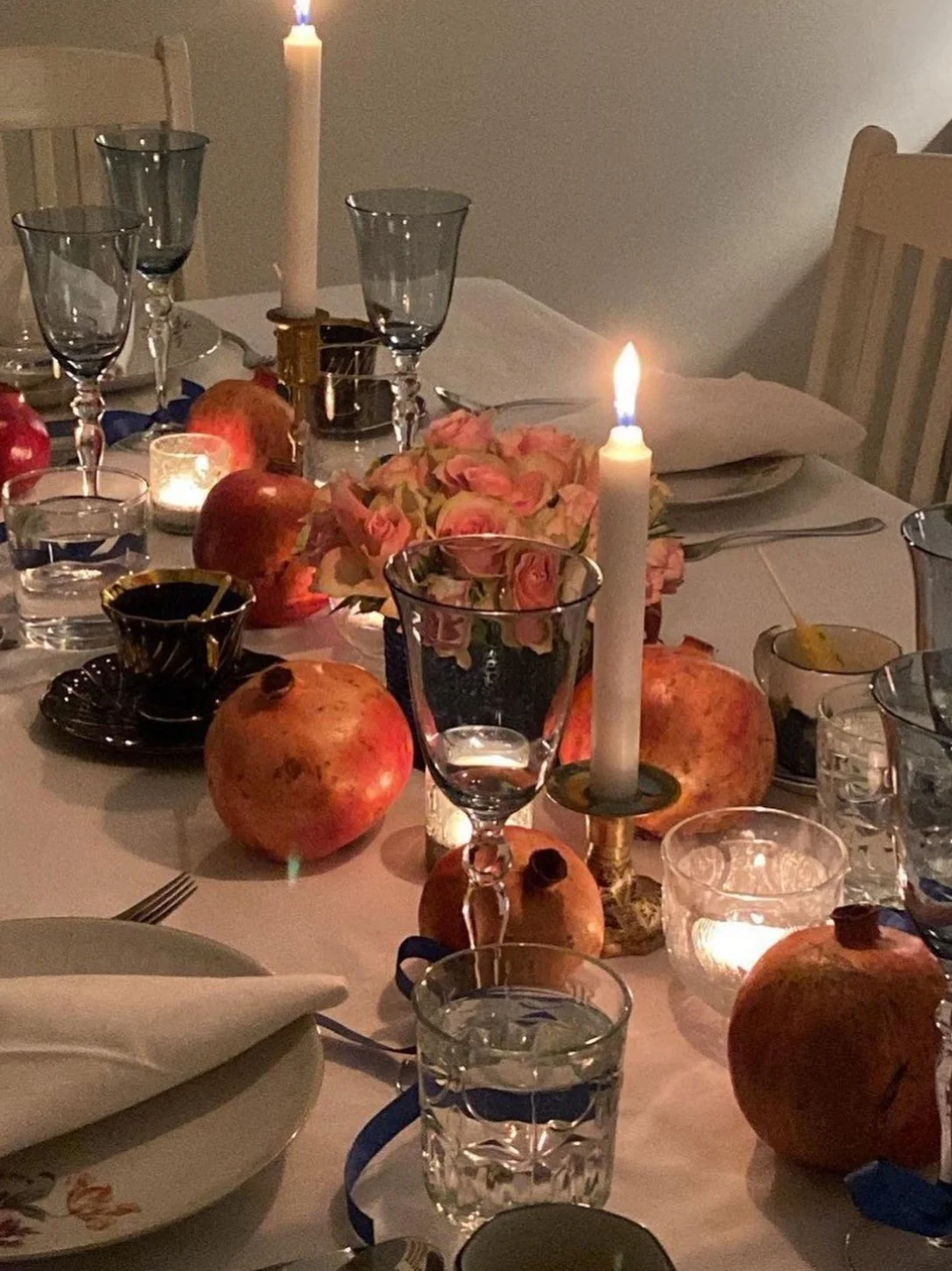 A dinner table decorated with pomegranates, candles, a bouquet of pink roses, wine glasses, and place settings, creating an elegant and warm atmosphere.