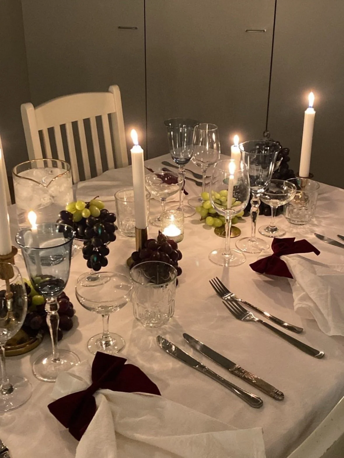 A decorated dining table set for a formal meal with candles, wine glasses, and grape-themed centerpieces.