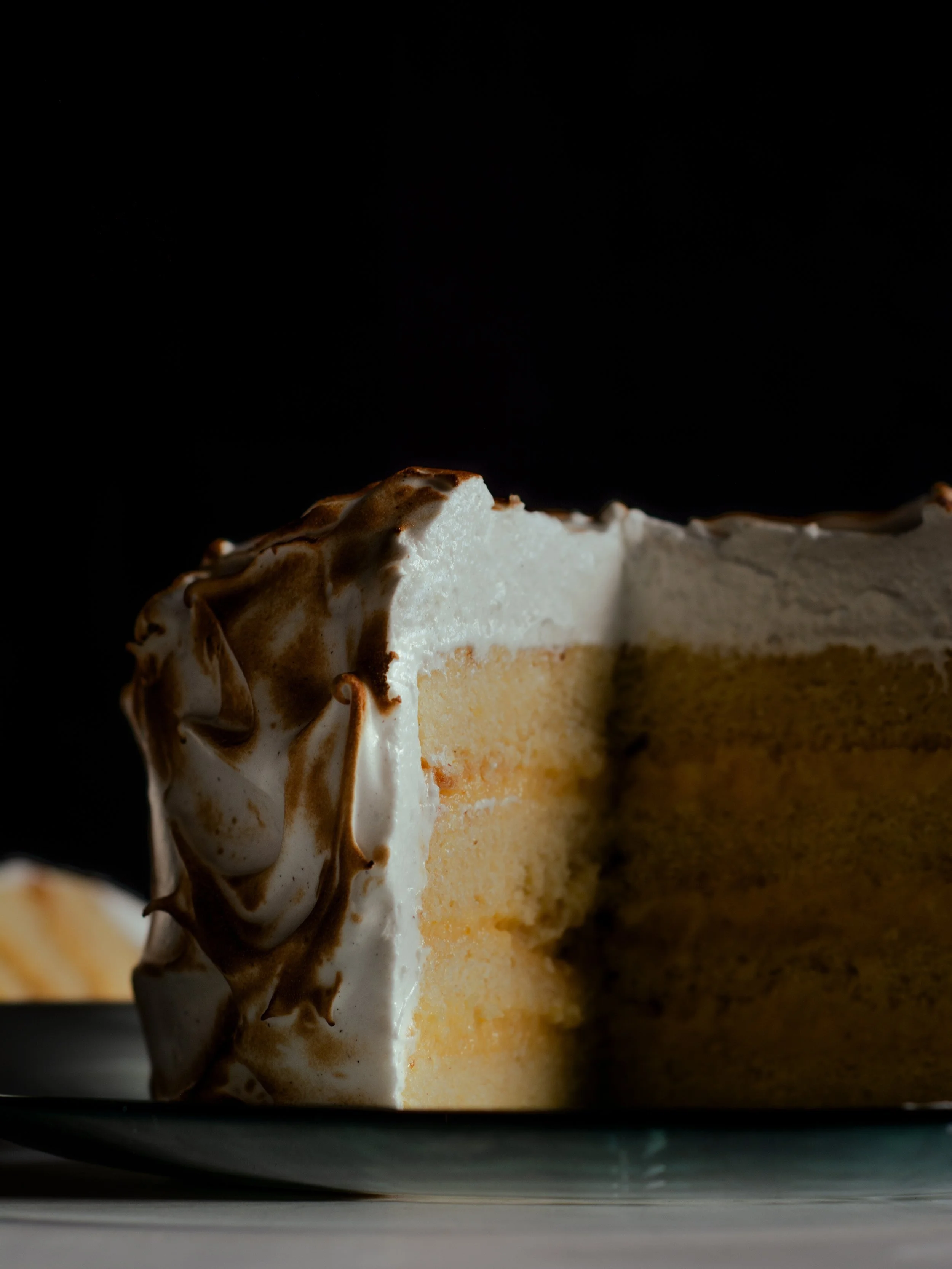 Close-up of a slice of vanilla cake with white frosting and chocolate swirls, on a black background.