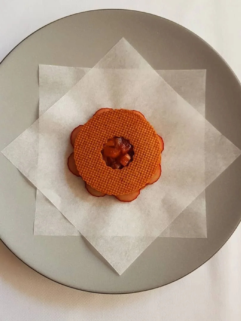 A round, orange dessert with a textured surface on top, placed on white parchment paper on a gray plate.
