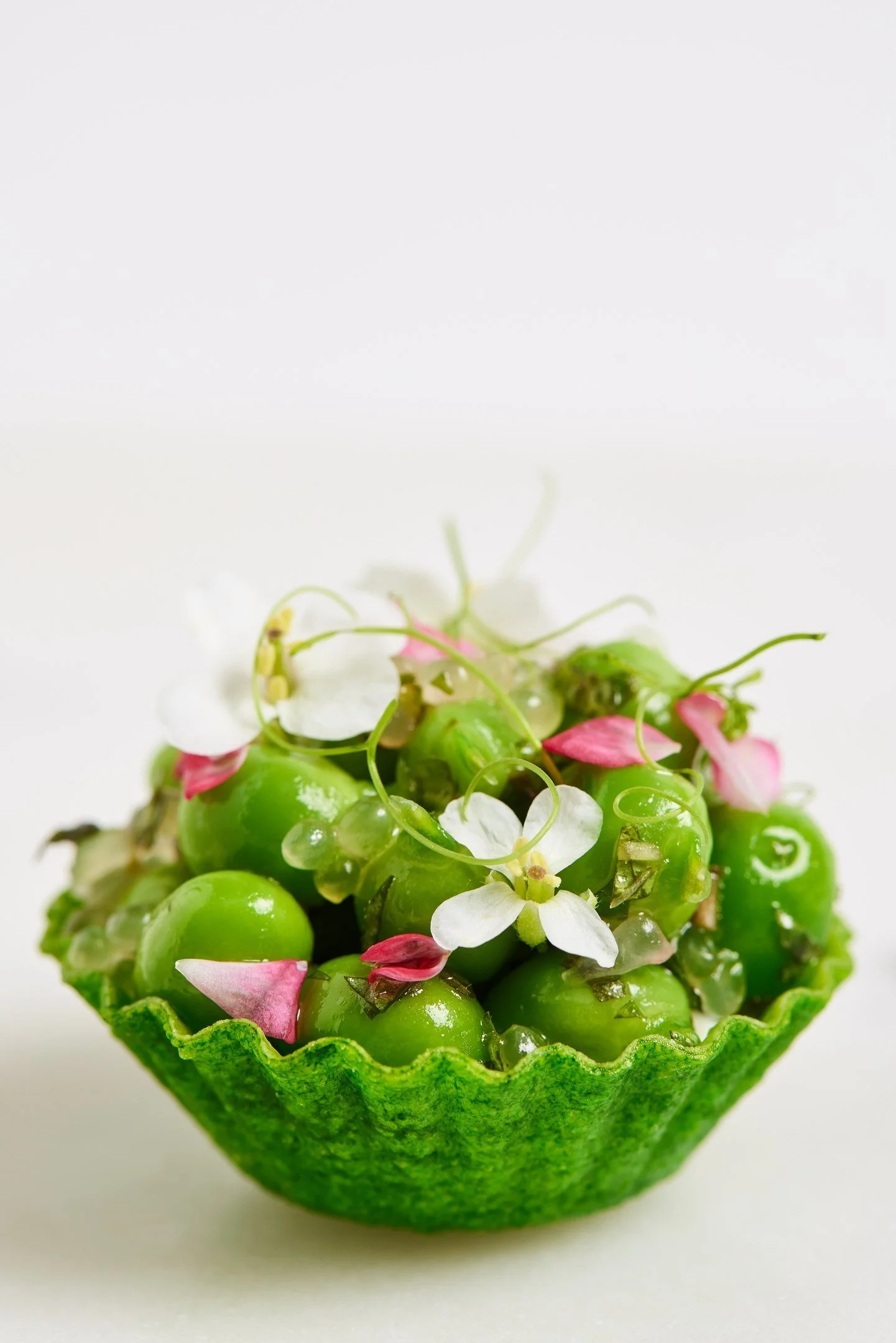 Green grapes served in a green fruit shell with edible flowers and petals, on a white background.