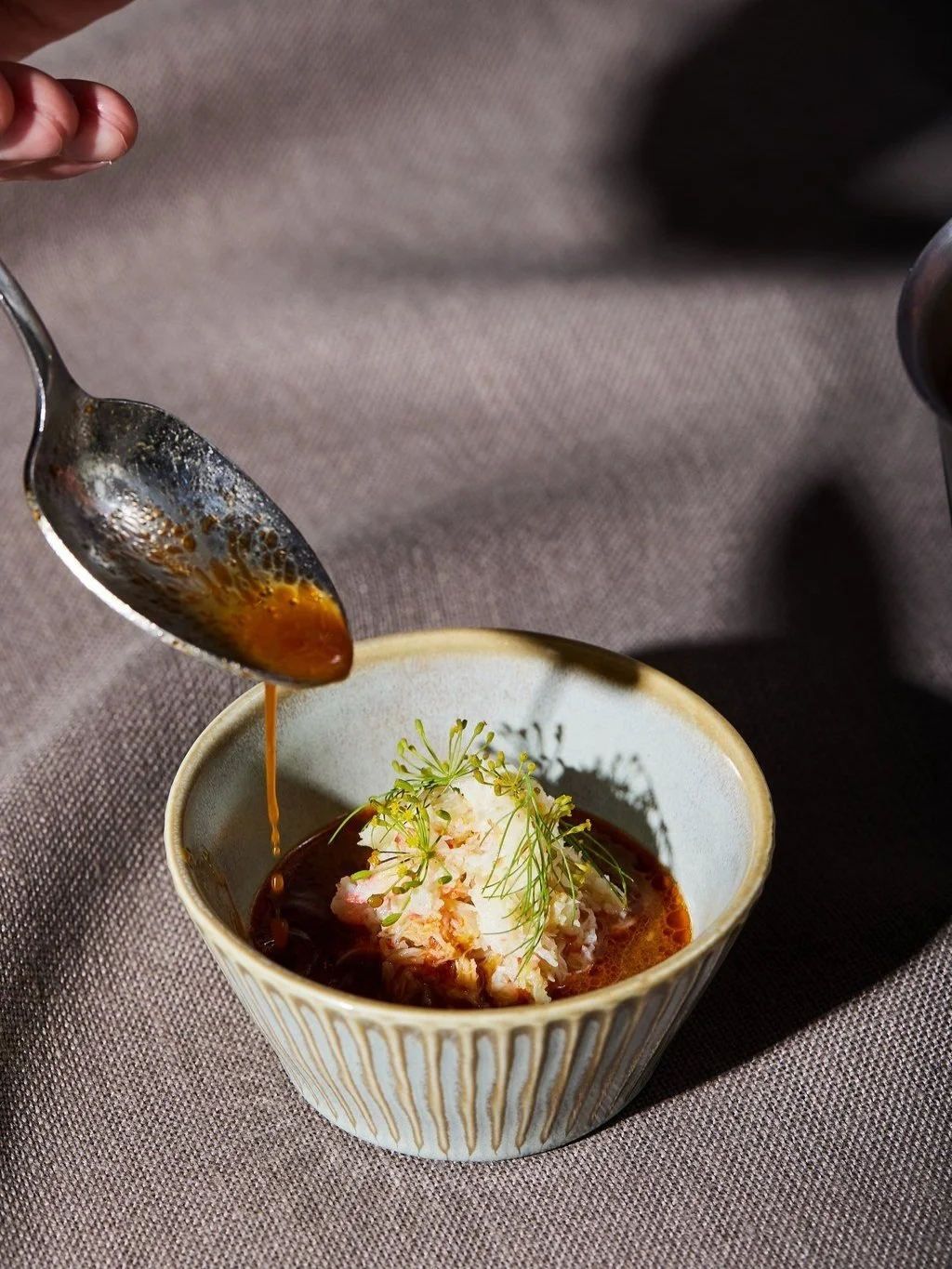 A spoon pouring sauce over a dish of crab meat garnished with herbs in a ceramic bowl.