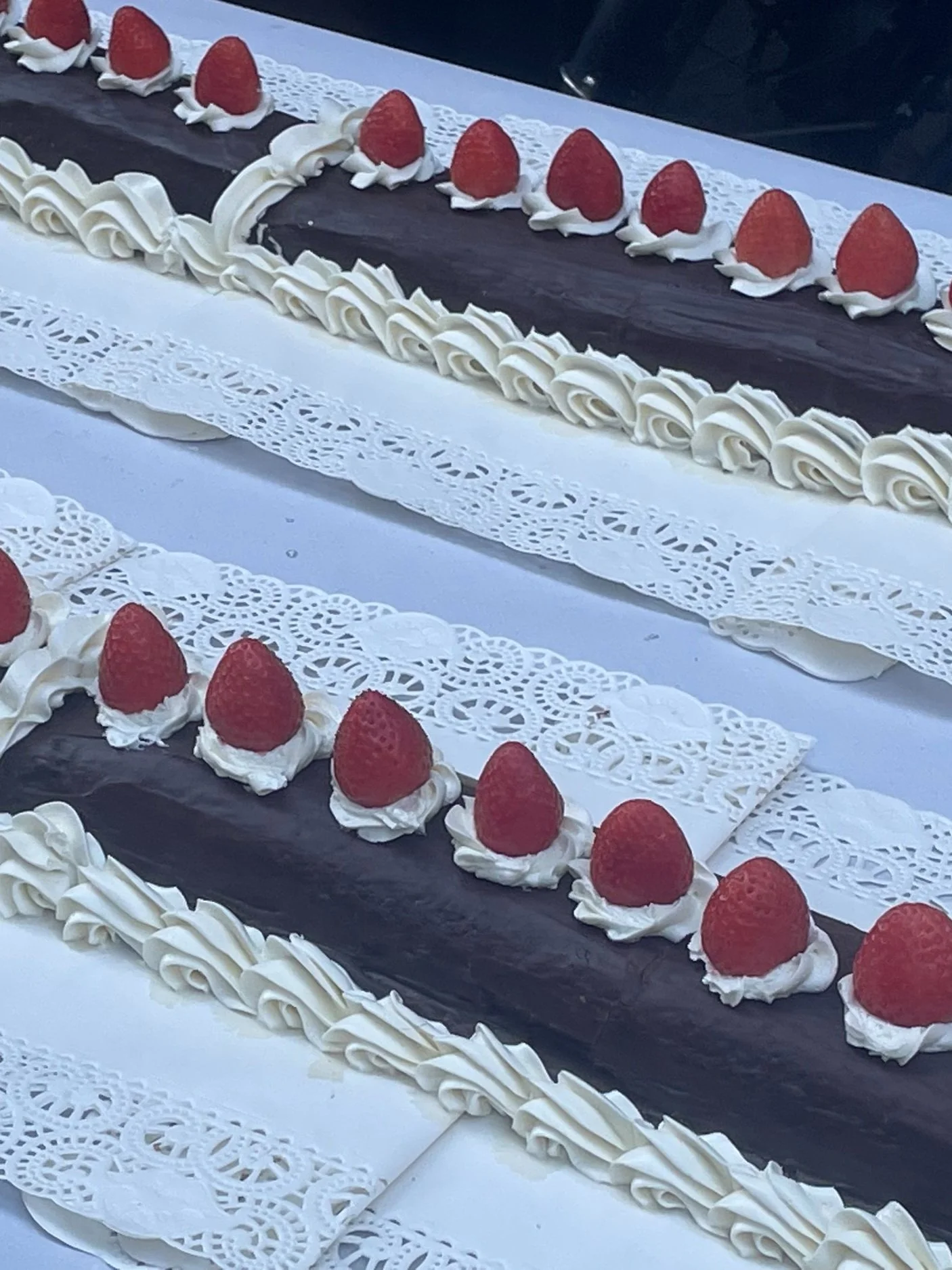 Long rectangular chocolate cakes decorated with white icing rosettes and strawberries on top.