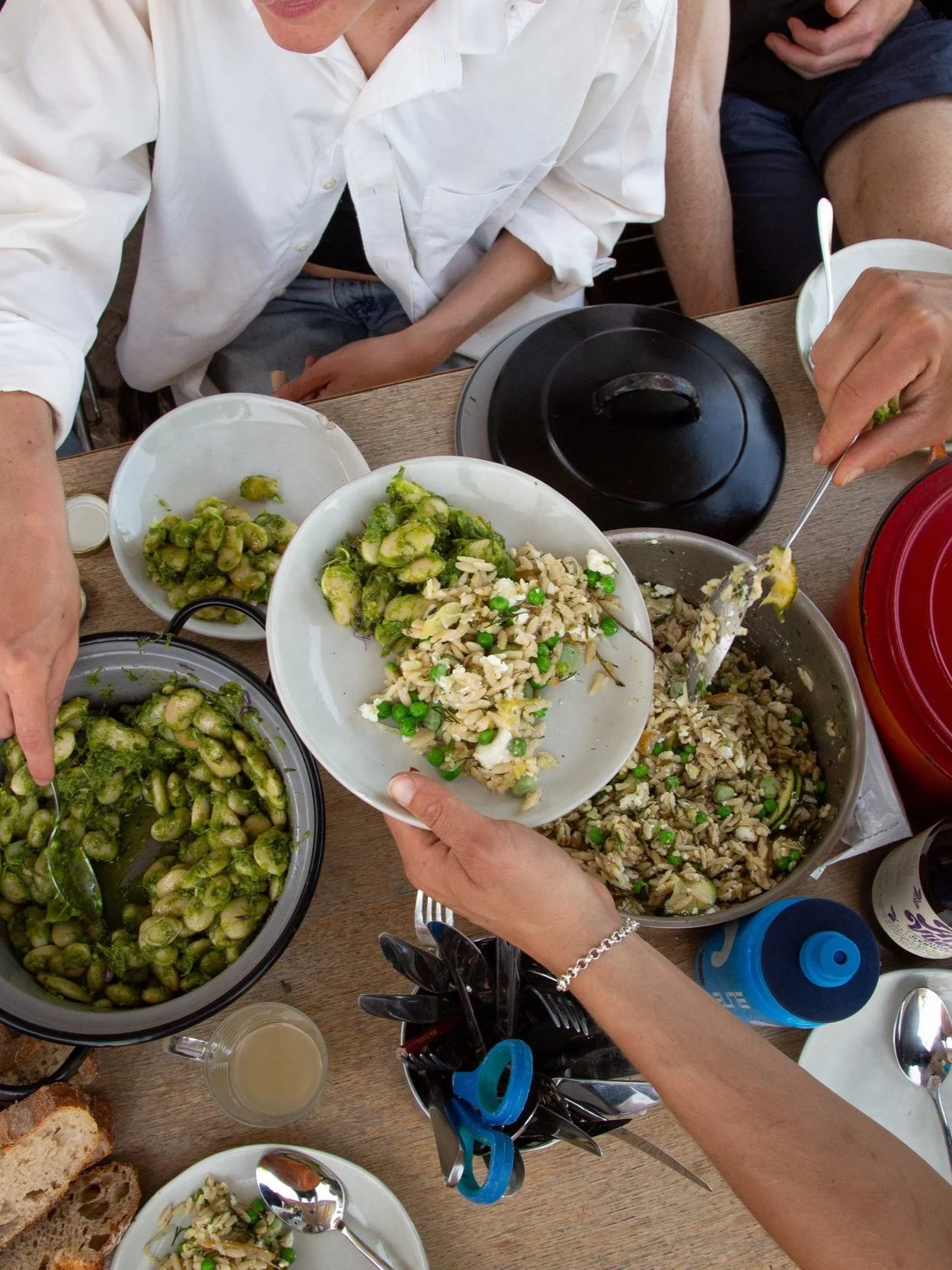 A group of people serving themselves food at a table with dishes of pasta, salad, and bread.
