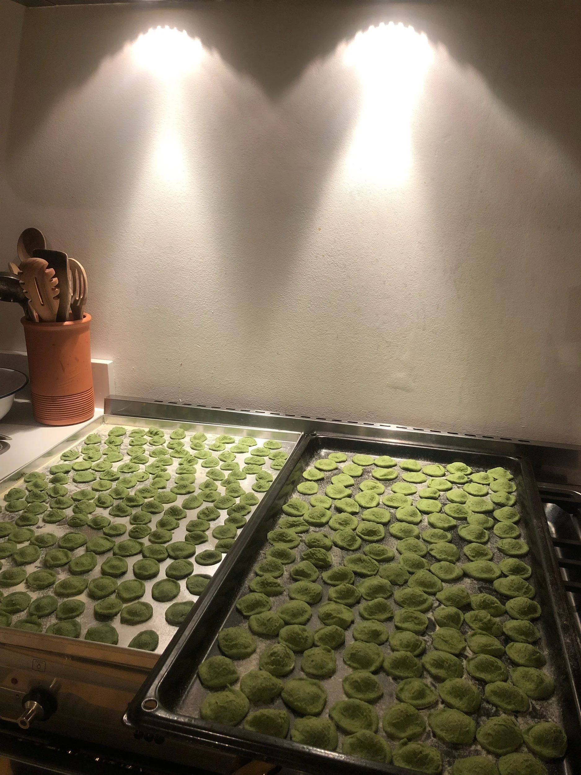Baking trays filled with small, round, green cookies on a kitchen counter under warm lighting.