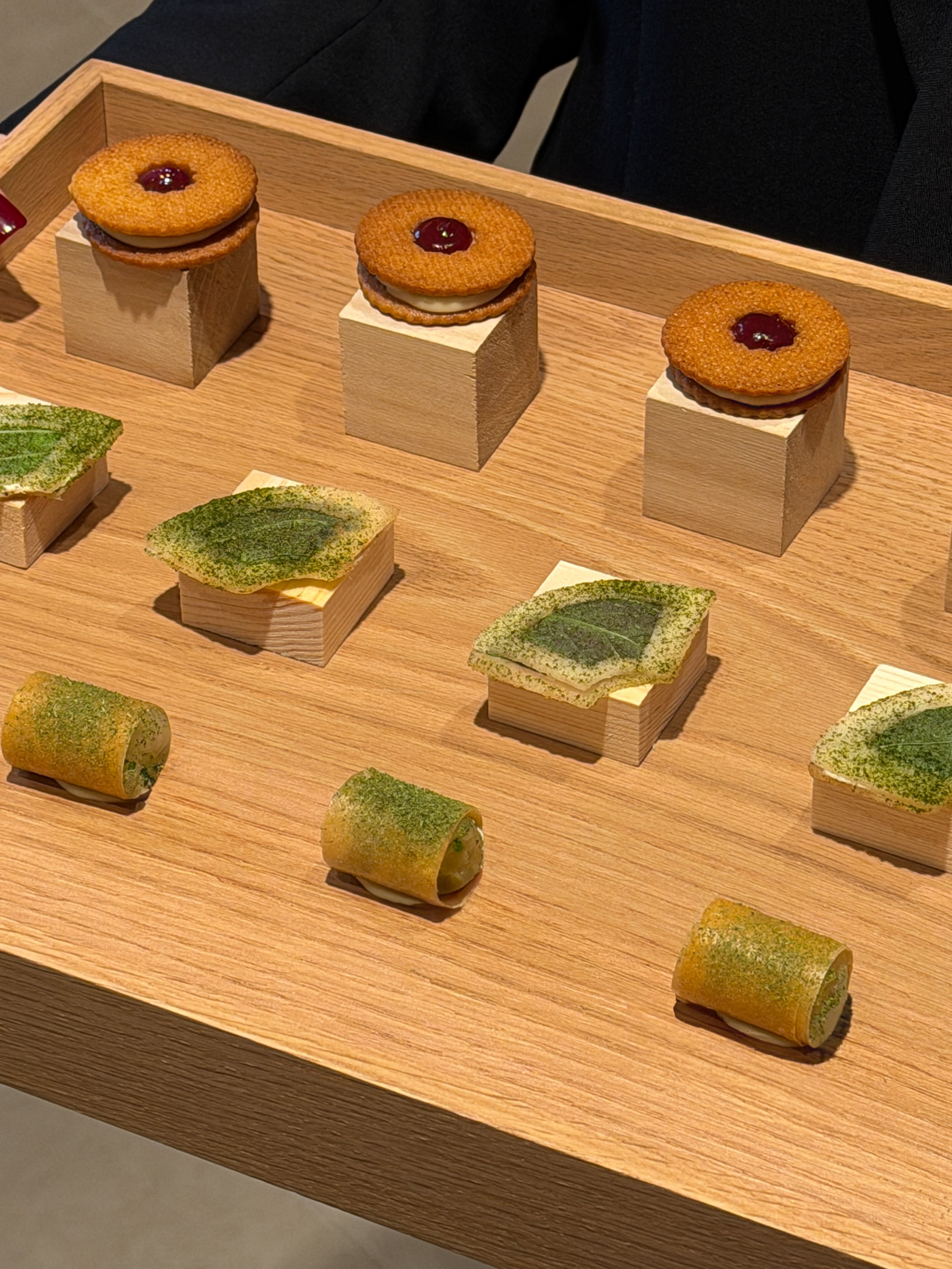 Assorted miniature desserts arranged on a wooden tray, including layered cakes, rolled pastries, and topped biscuits.