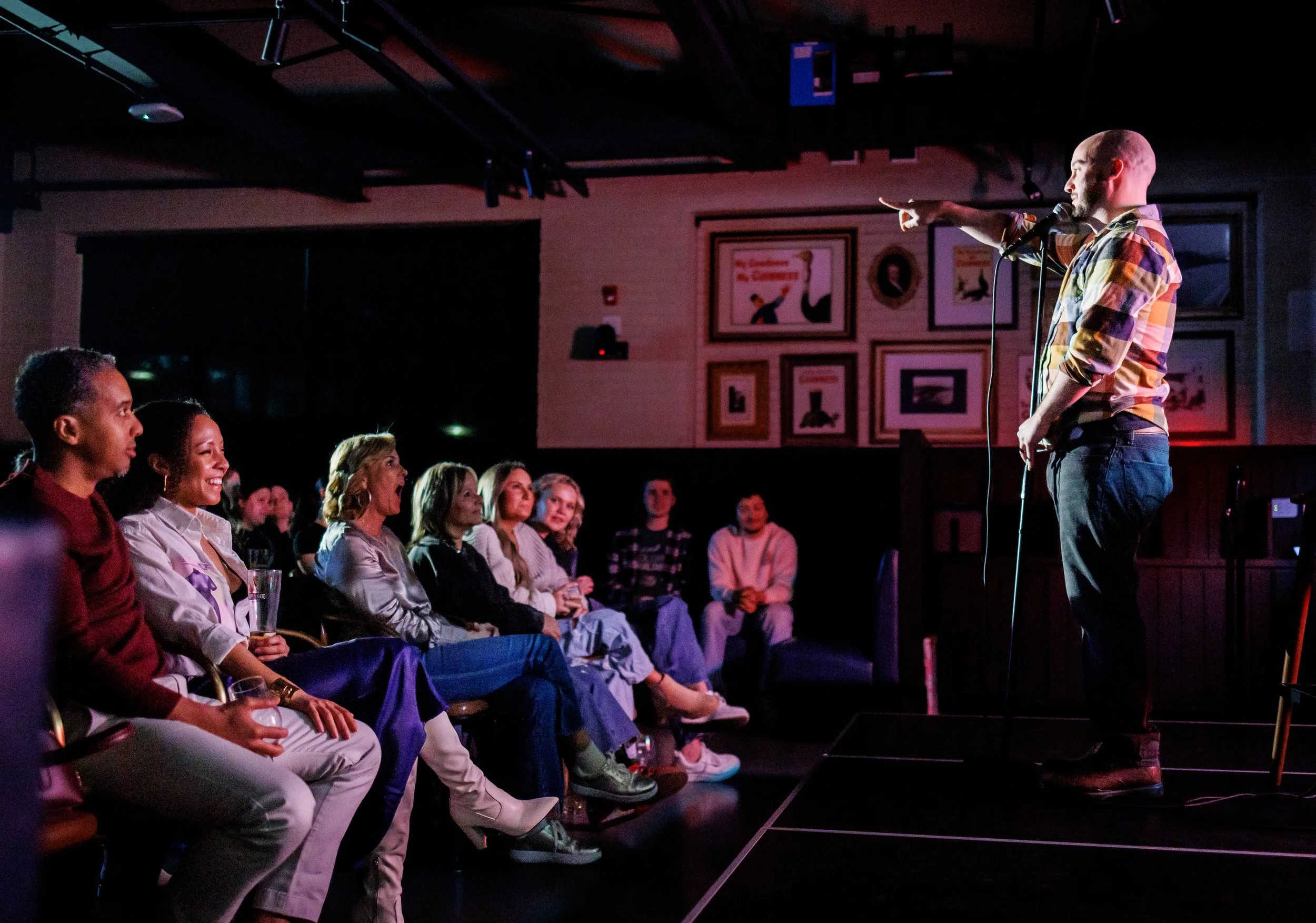 A comedian performing on stage at a comedy club with an audience of women laughing and enjoying the show.