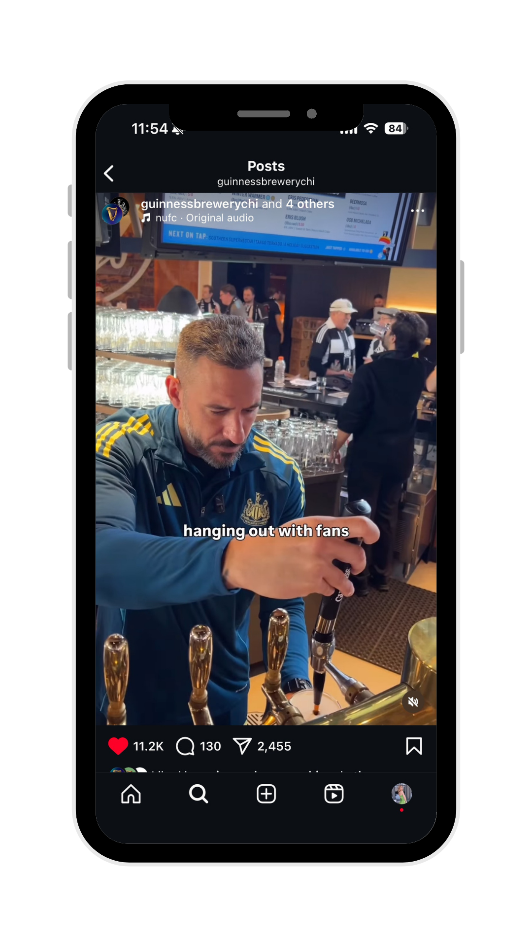 A man in a blue sports jacket with yellow stripes and a Newcastle United logo pours beer from a tap at a bar, with other people and bar equipment in the background.