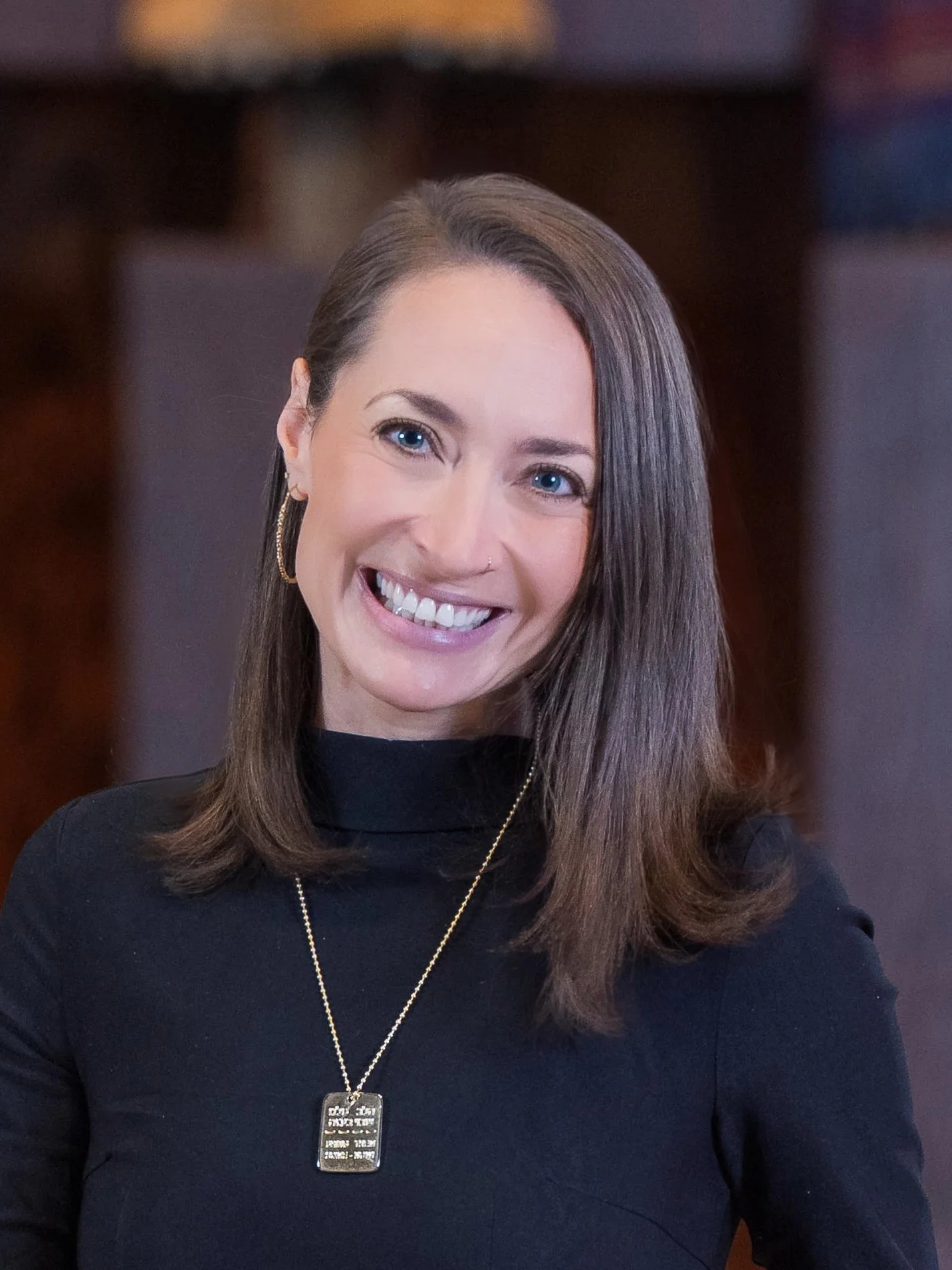 Senior Rabbi Emily Hyatt standing in front of a sand-colored brick wall, wearing a black shirt..