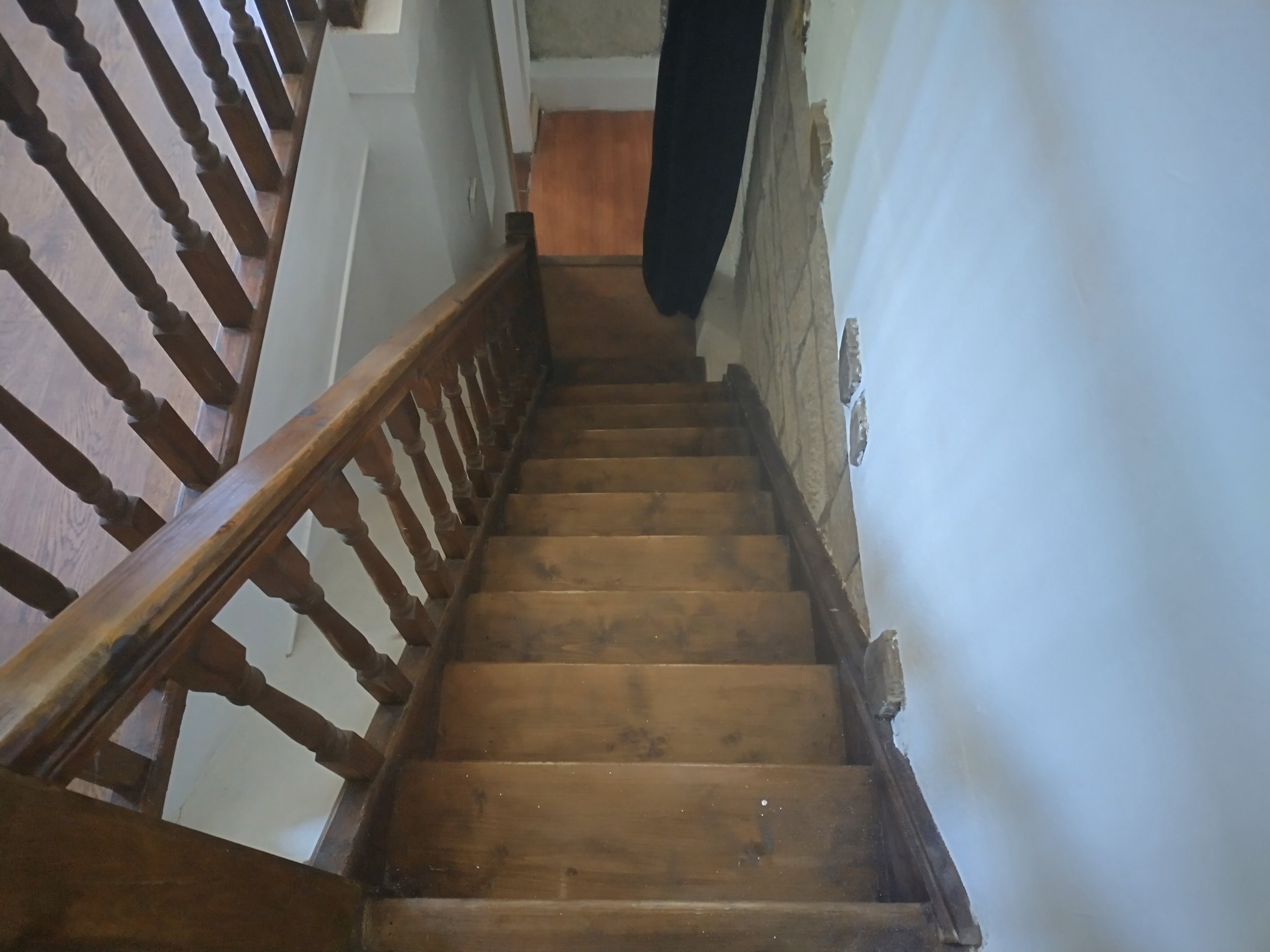 Wooden staircase with railing, light walls, and a stone accent wall.