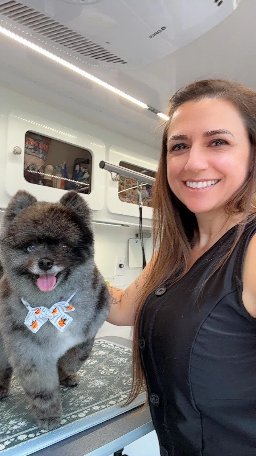 Smiling woman taking a selfie with a fluffy puppy on an examination table inside a veterinary clinic.