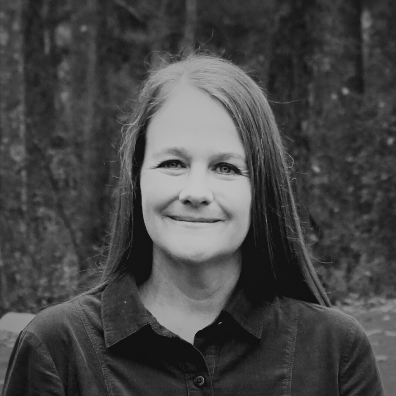 Family of five smiling outdoors in autumn, with trees displaying fall colors in the background.