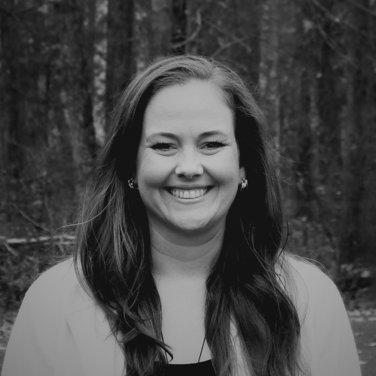Three smiling women standing together indoors, one in a hat and denim jacket, another with hoop earrings and a patterned dress, and the third with a nickname tag and a green floral dress, with colorful flowers behind them.